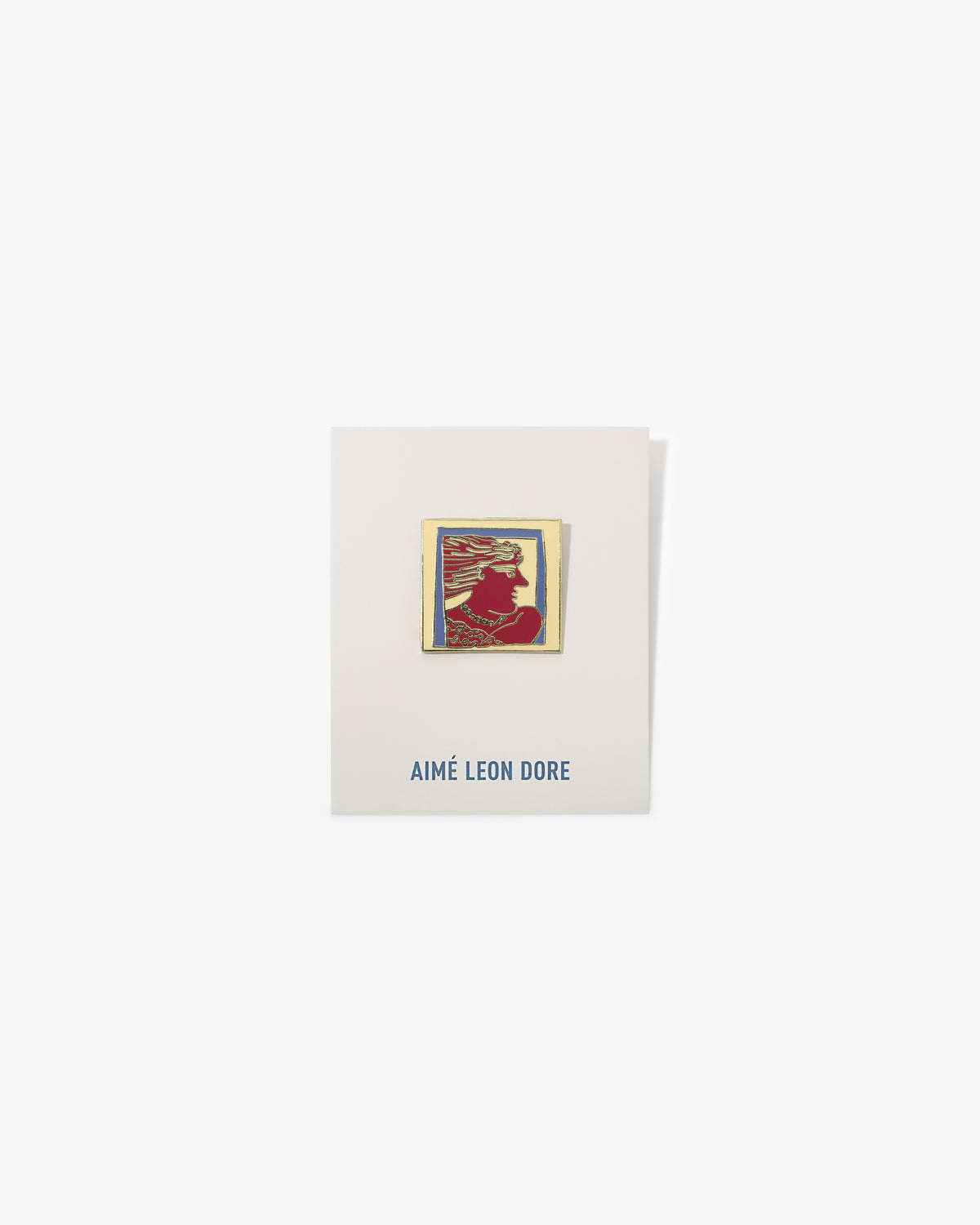 A gold-framed red and yellow Graphic Pin with a silhouette on a white AIMÉ LEON DORE card.