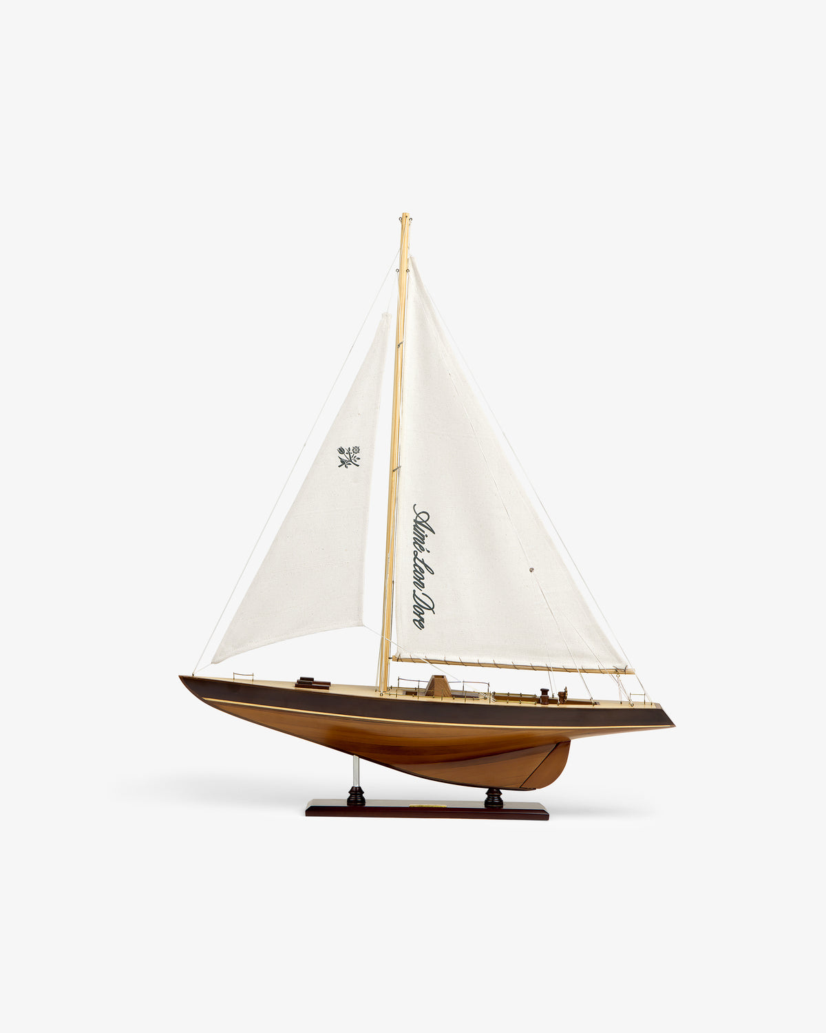 The Walnut Model Sailboat features white sails and comes displayed on a stand against a plain white background.