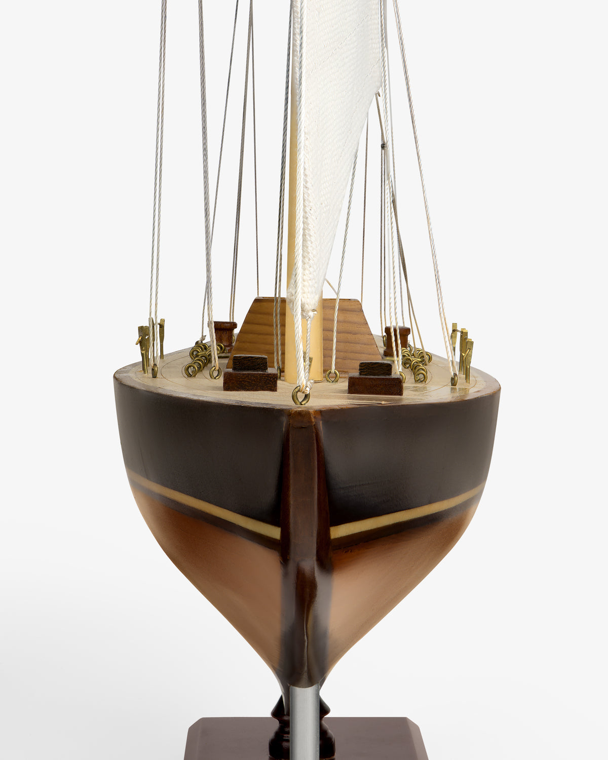 Walnut Model Sailboat viewed from the front, featuring a brown hull, deck details, and a white sail with rigging.