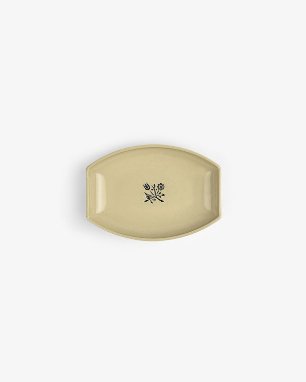 The Crest Catchall: a small beige ceramic dish with a black floral design at its center, shown from above.