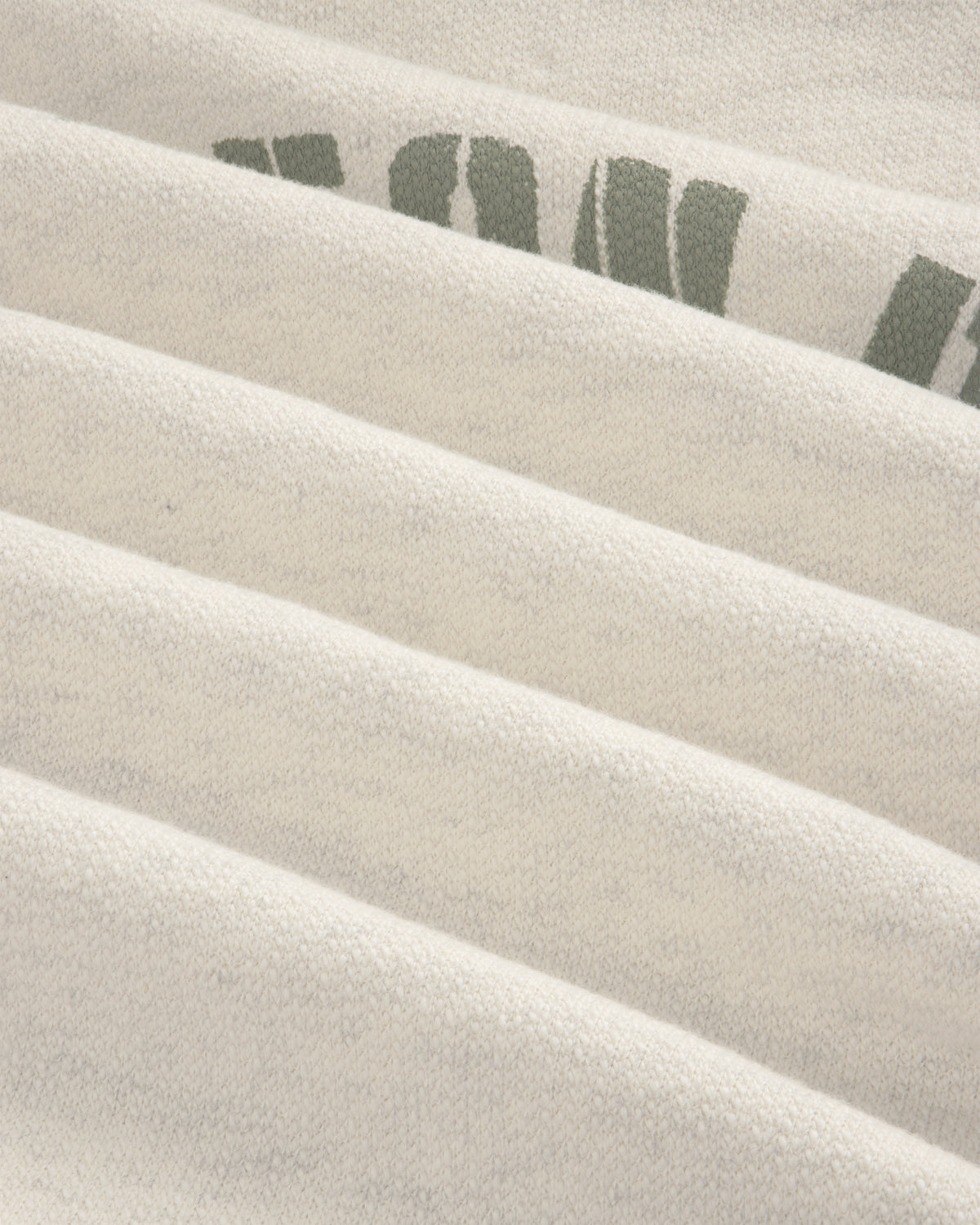 Close-up of Dock Hoodie’s light fabric with faint green text, showing soft texture and horizontal folds.