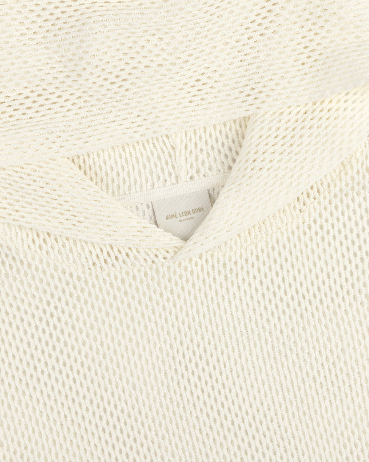 Close-up of an off-white Open Mesh Hoodie with textured knit fabric and a visible neck label reading Aime Leon Dore.