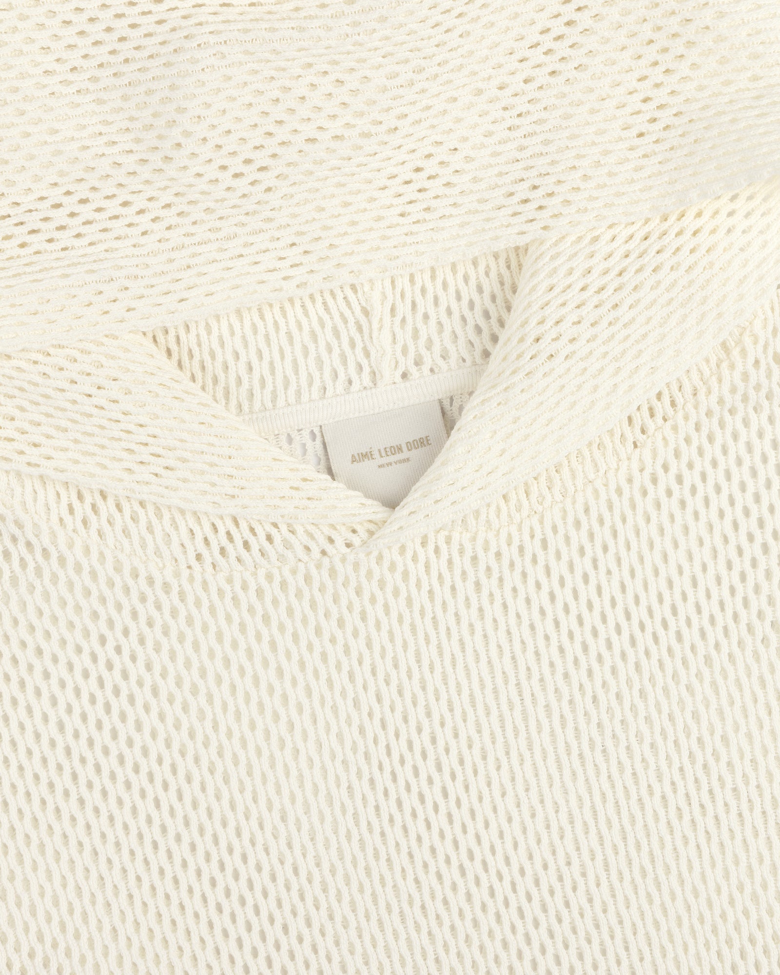 Close-up of an off-white Open Mesh Hoodie with textured knit fabric and a visible neck label reading Aime Leon Dore.
