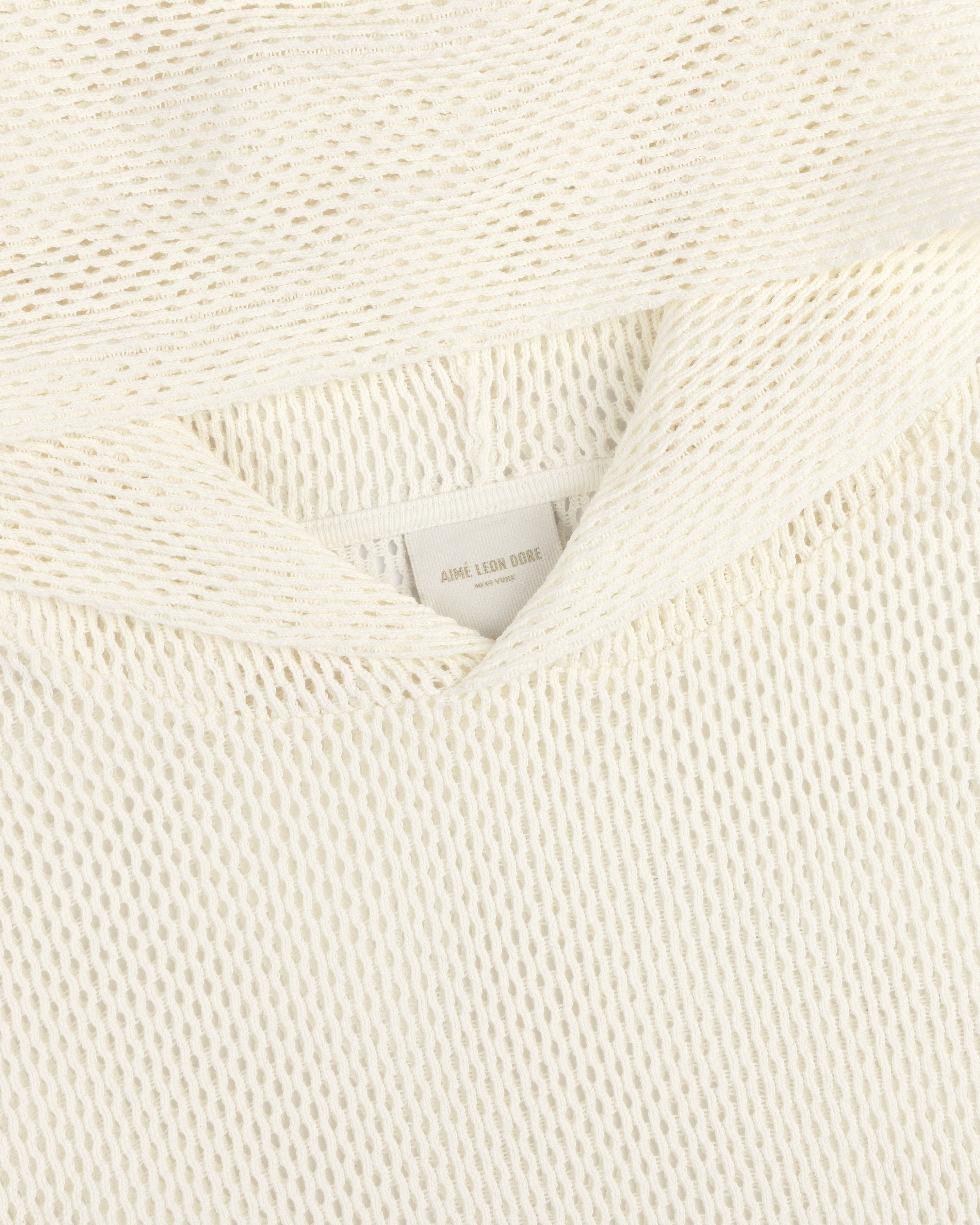 Close-up of an off-white Open Mesh Hoodie with textured knit fabric and a visible neck label reading Aime Leon Dore.