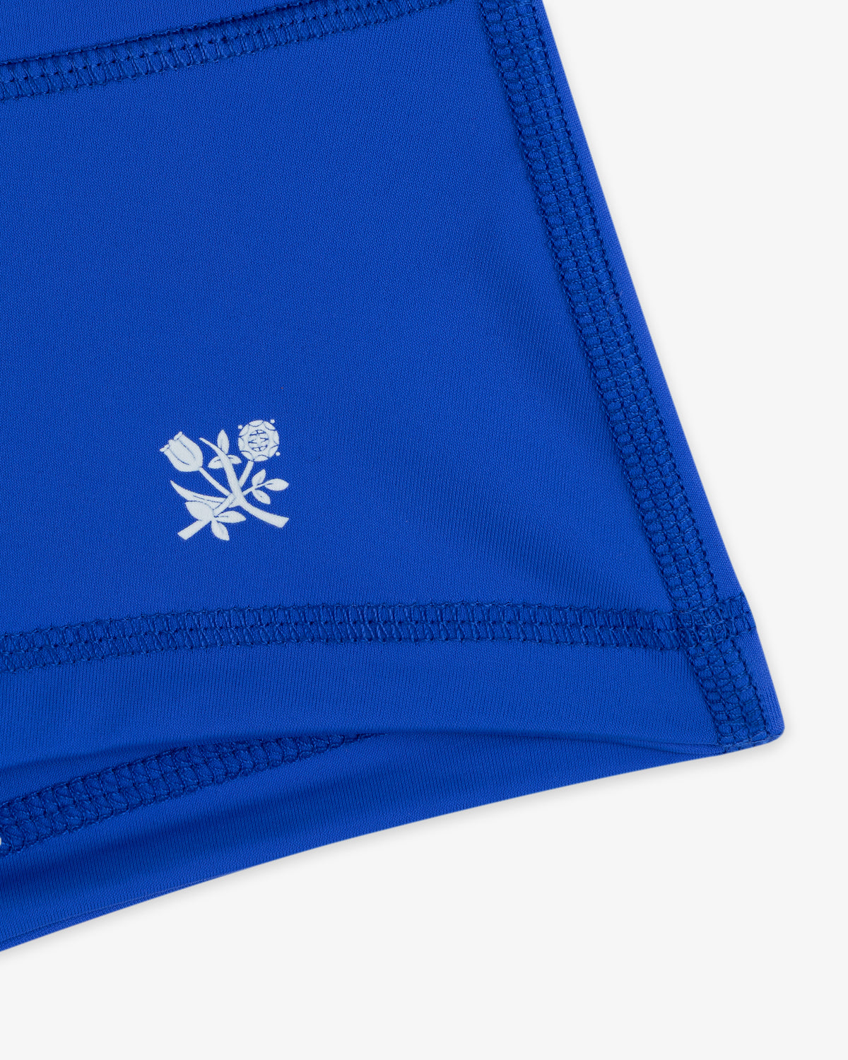 Close-up of Crest Swim Short's blue fabric with dark stitching and a small white floral logo.