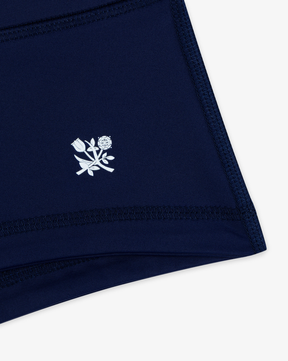 Crest Swim Short in navy blue fabric with white stitched outline and a small white floral graphic near the hem.