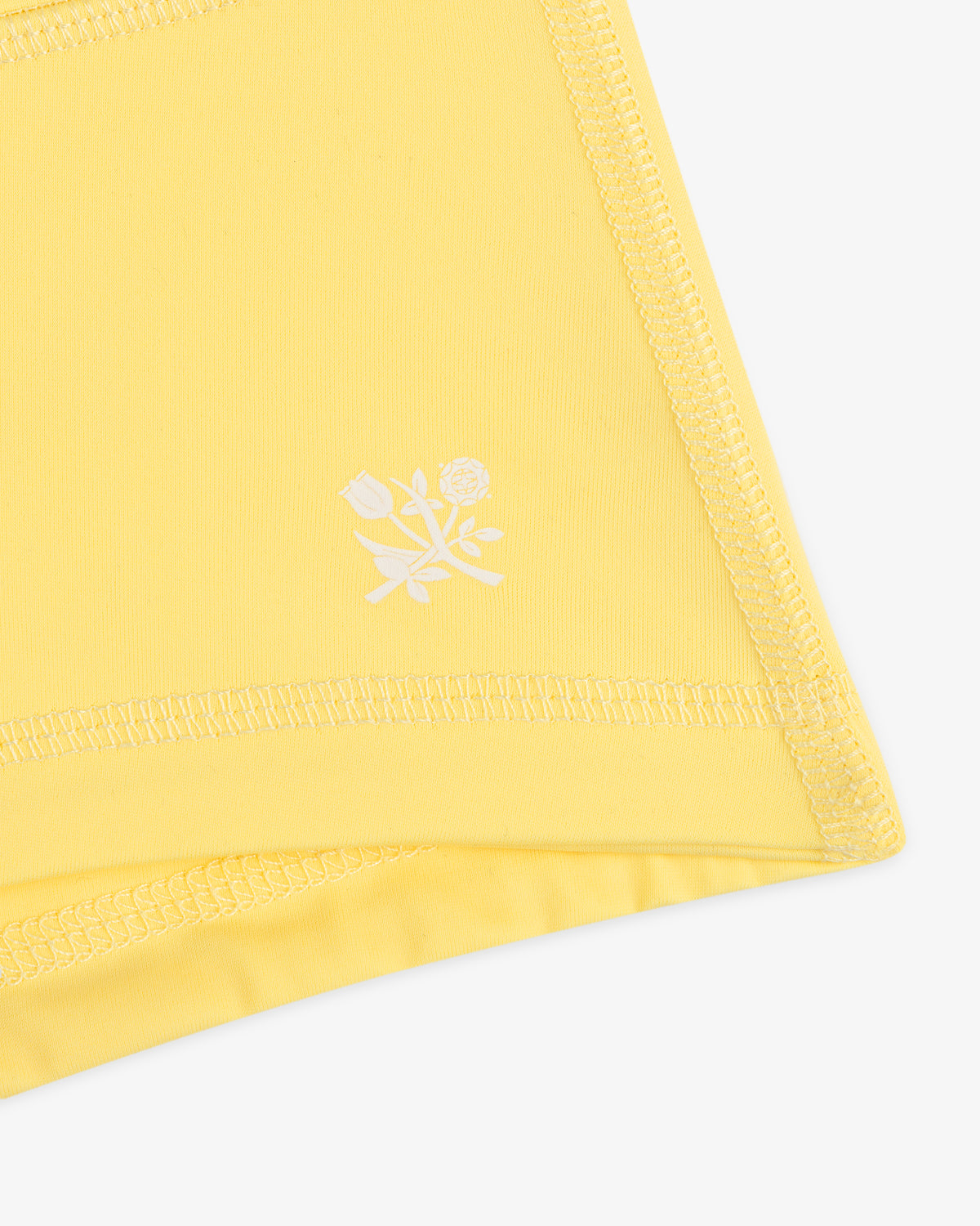 Close-up of Crest Swim Short's yellow fabric with visible stitching and a small white floral graphic.