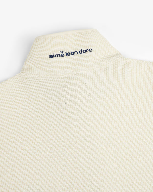 Close-up of the ALD Golf Piqué Full Zip Sweater's cream ribbed collar with navy aime leon dore embroidery on back.