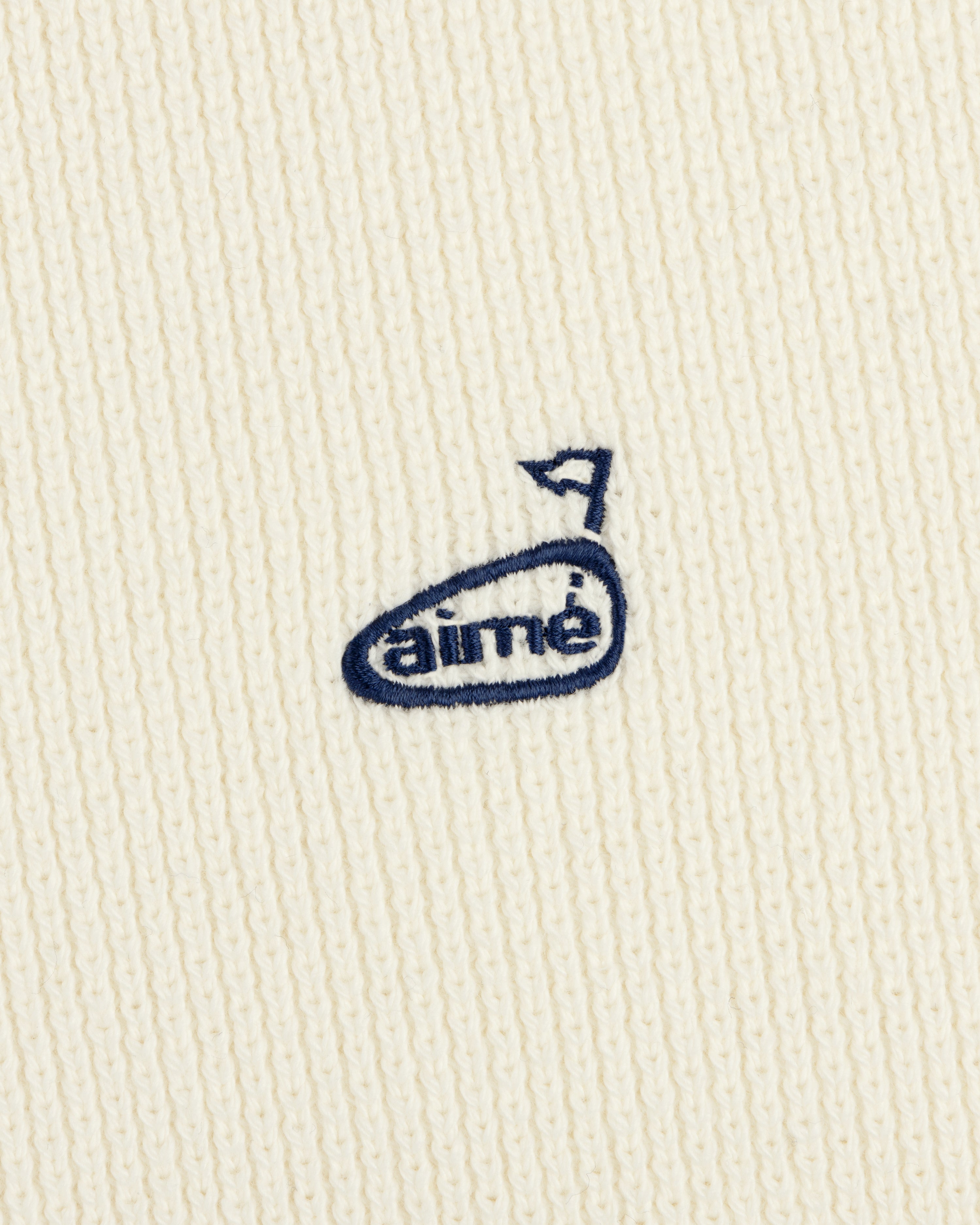 The ALD Golf Piqué Full Zip Sweater features white ribbed fabric and a small blue embroidered aimé logo with an arrow above the "e".