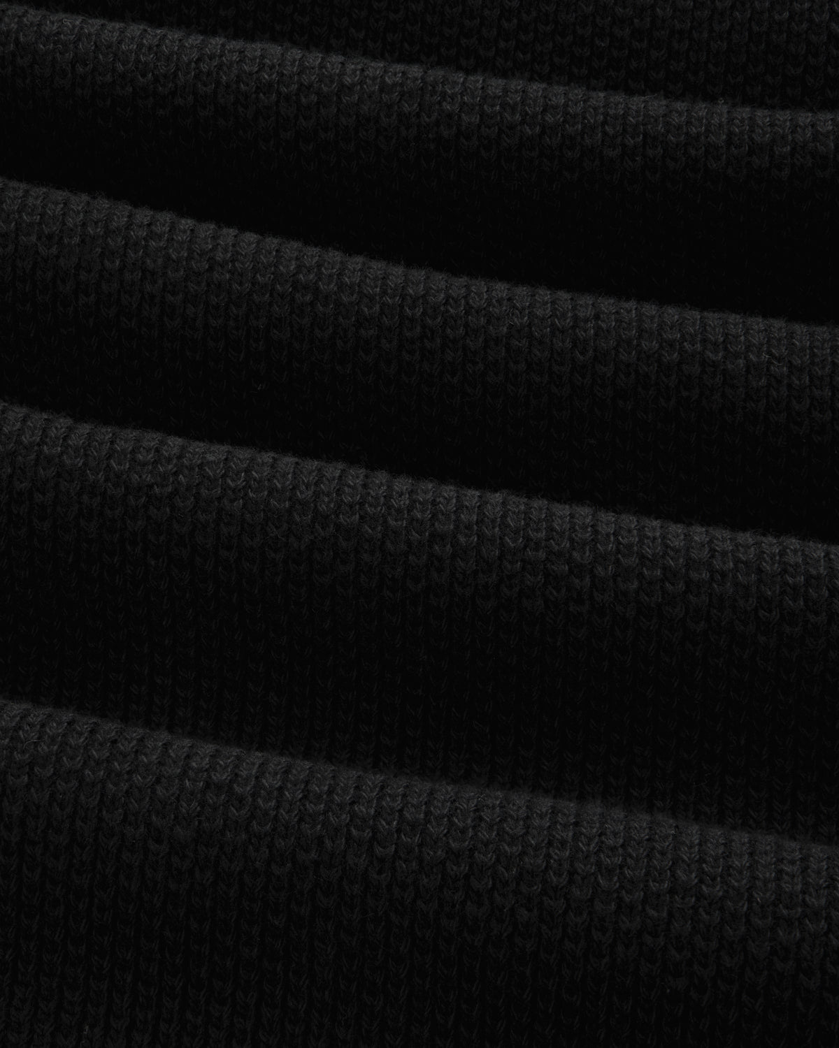 Close-up of the ALD Golf Piqué Full Zip Sweater's folded black ribbed fabric with visible textured lines.