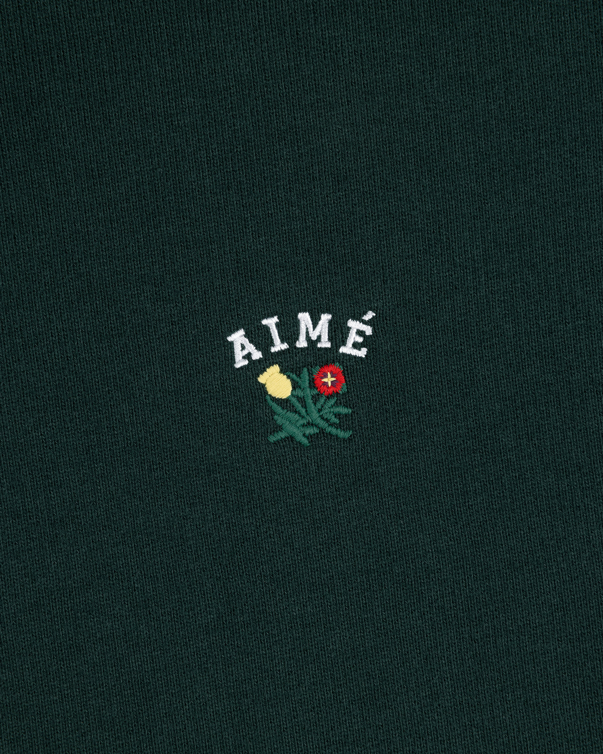 Dark green Crest Quarter Zip Pullover with AIMÉ embroidered above a yellow and red flower with green leaves.