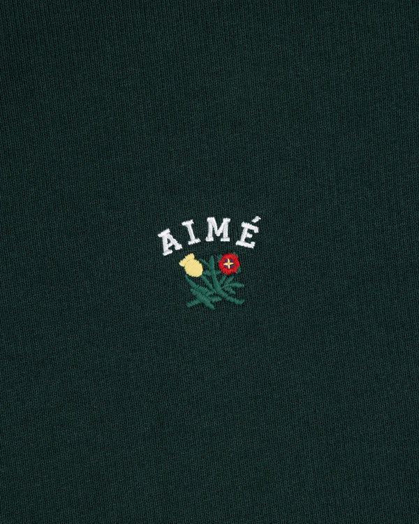 Dark green Crest Quarter Zip Pullover with AIMÉ embroidered above a yellow and red flower with green leaves.