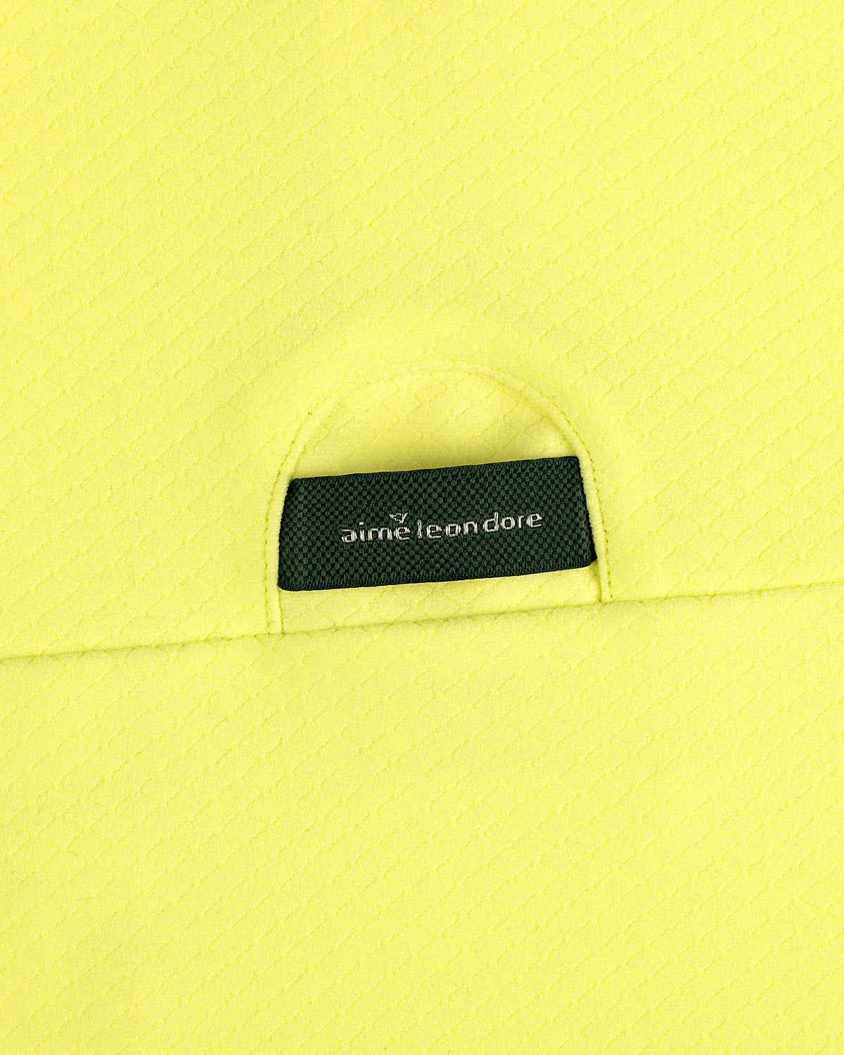 A close-up of an ALD Golf Quarter Zip Pullover’s black Aimé Leon Dore label sewn onto textured yellow fabric.