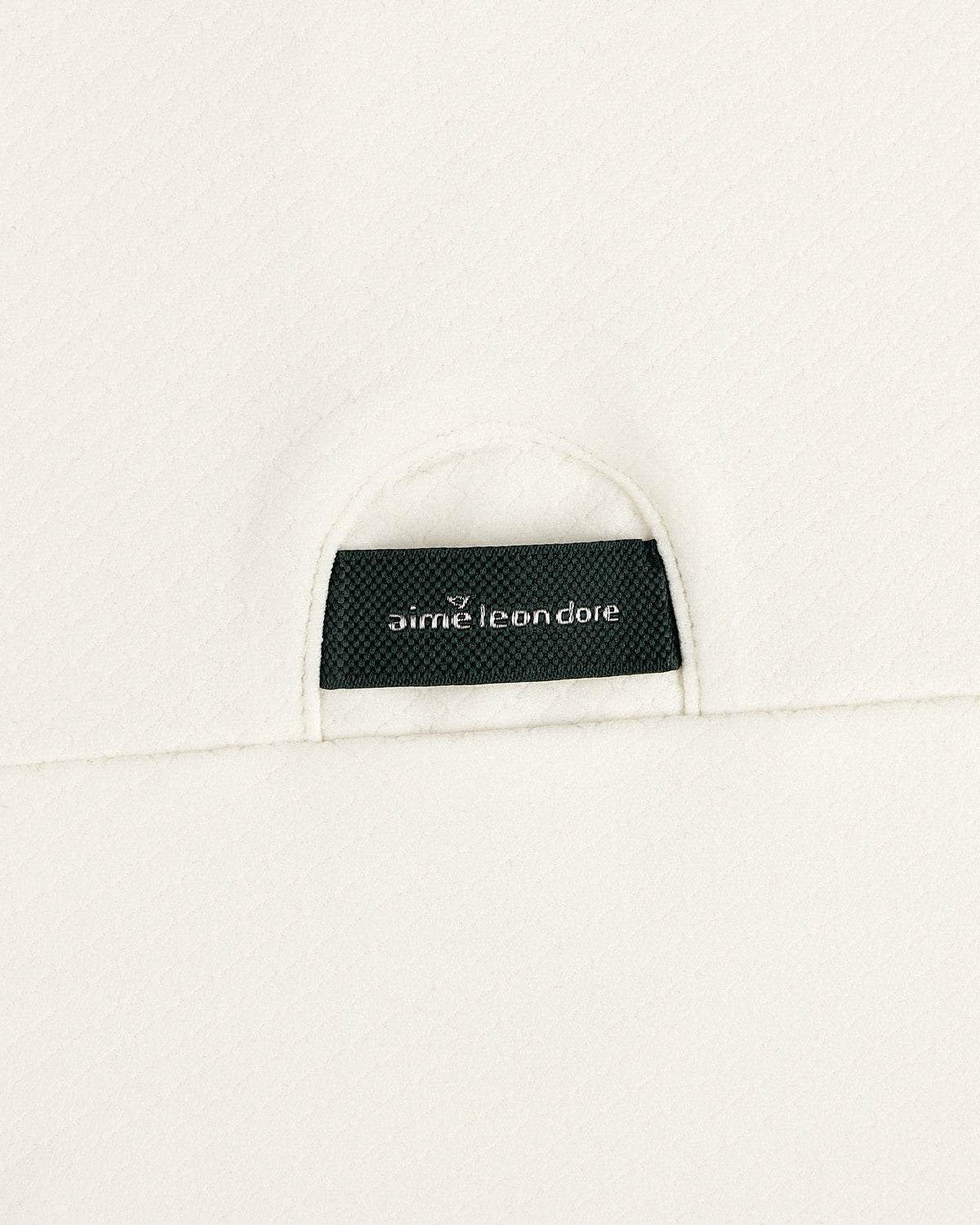 A black Aimé Leon Dore label sewn into the off-white ALD Golf Quarter Zip Pullover’s textured fabric.