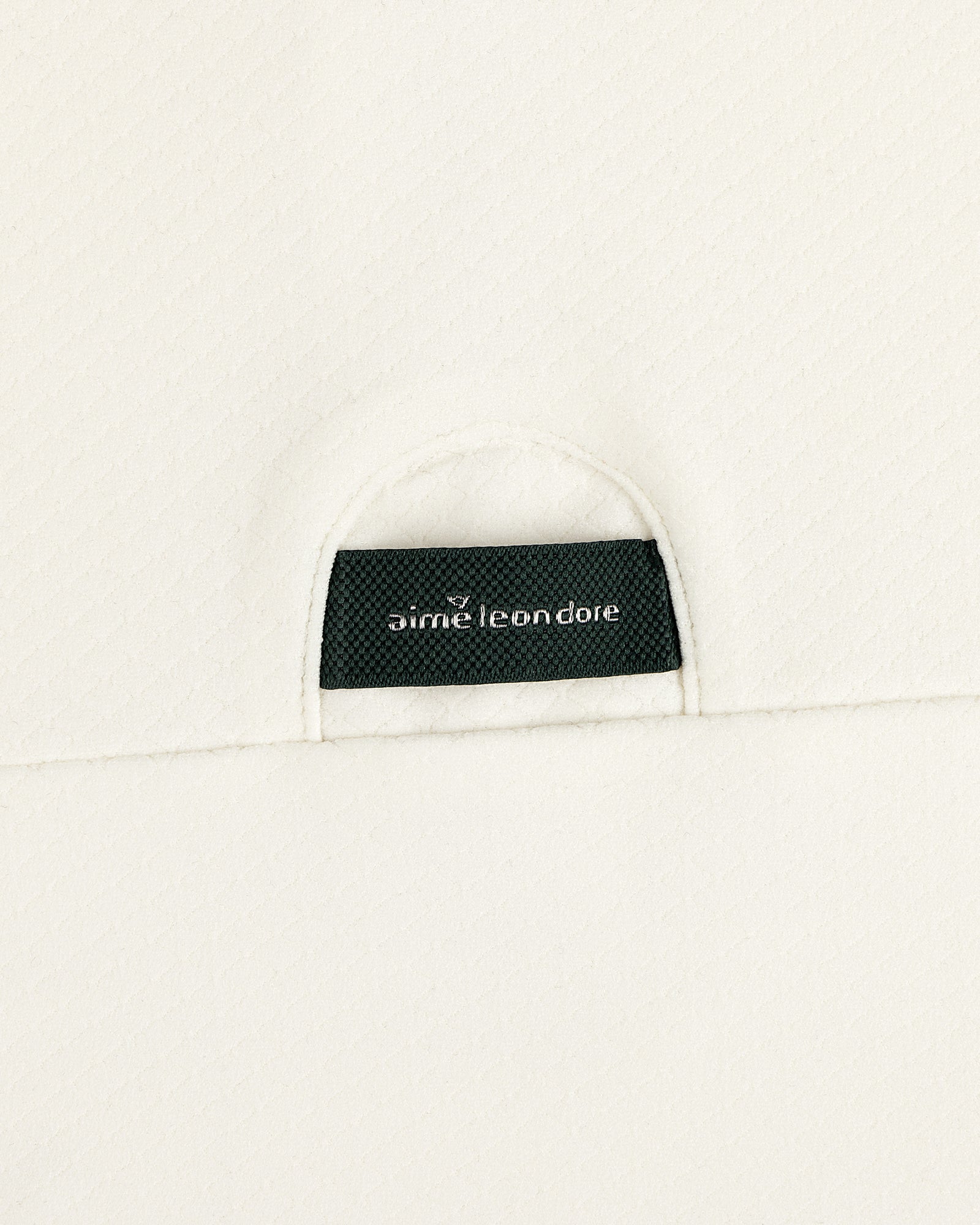 A black Aimé Leon Dore label sewn into the off-white ALD Golf Quarter Zip Pullover’s textured fabric.