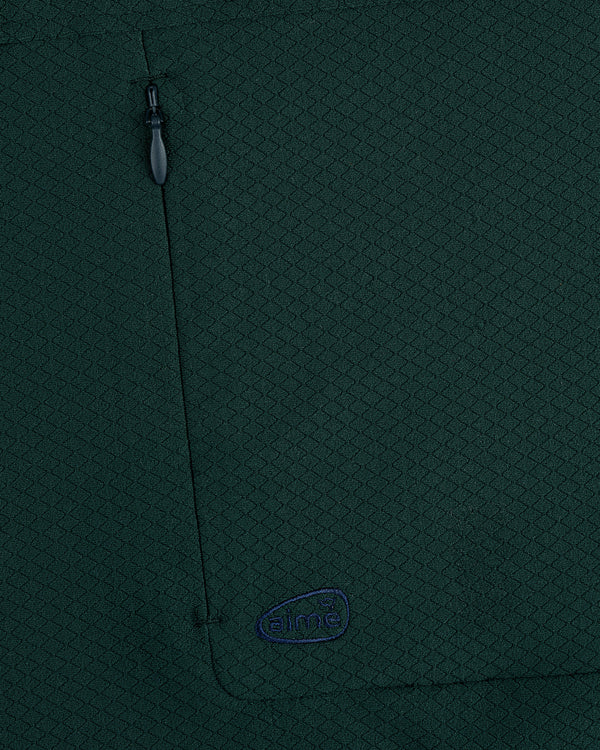 Close-up of ALD Golf Quarter Zip Pullover in dark green with textured fabric, zippered pocket, and small embroidered logo.