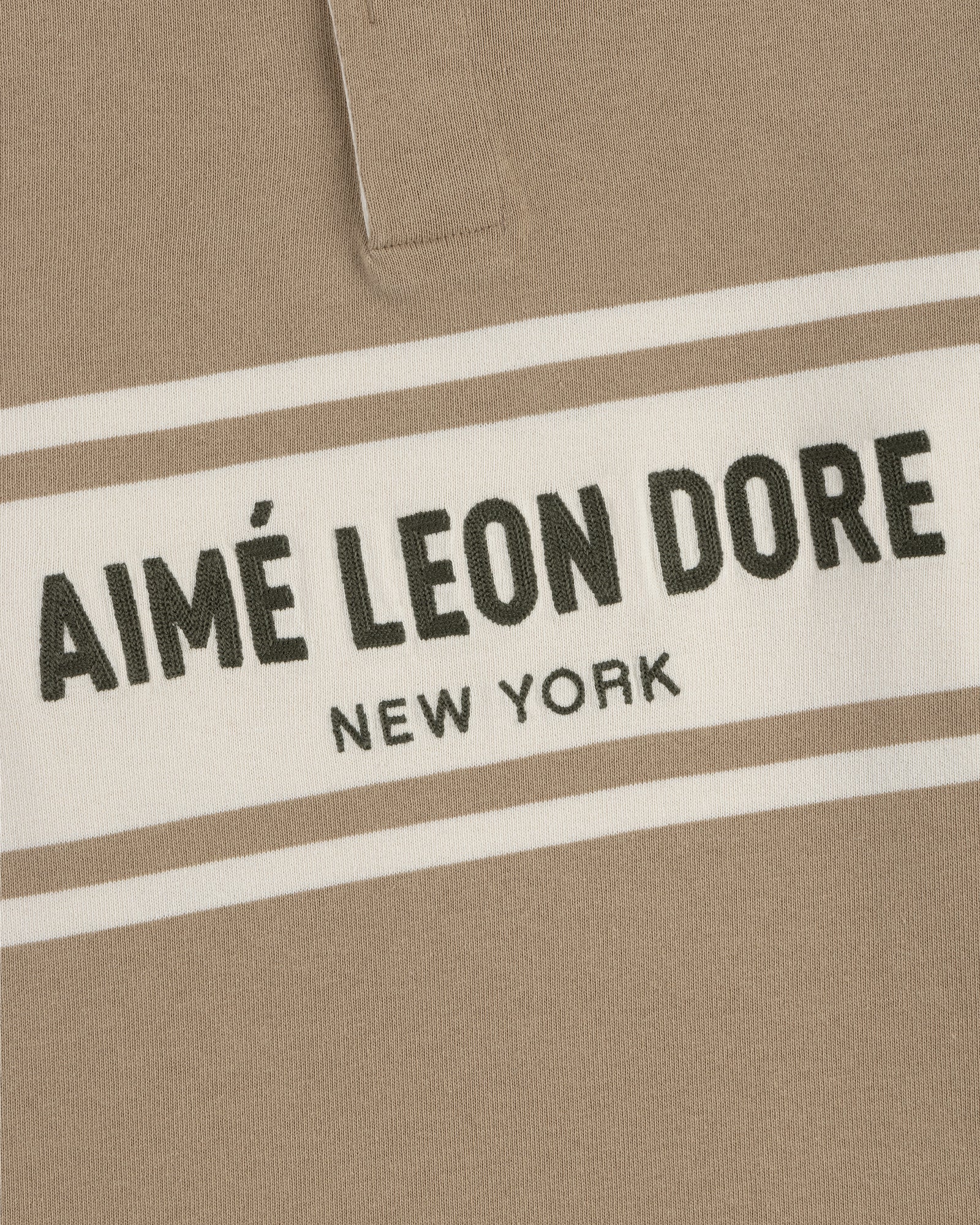 Close-up of a beige Chest Stripe Logo Rugby with AIMÉ LEON DORE NEW YORK in bold black on a white chest stripe.