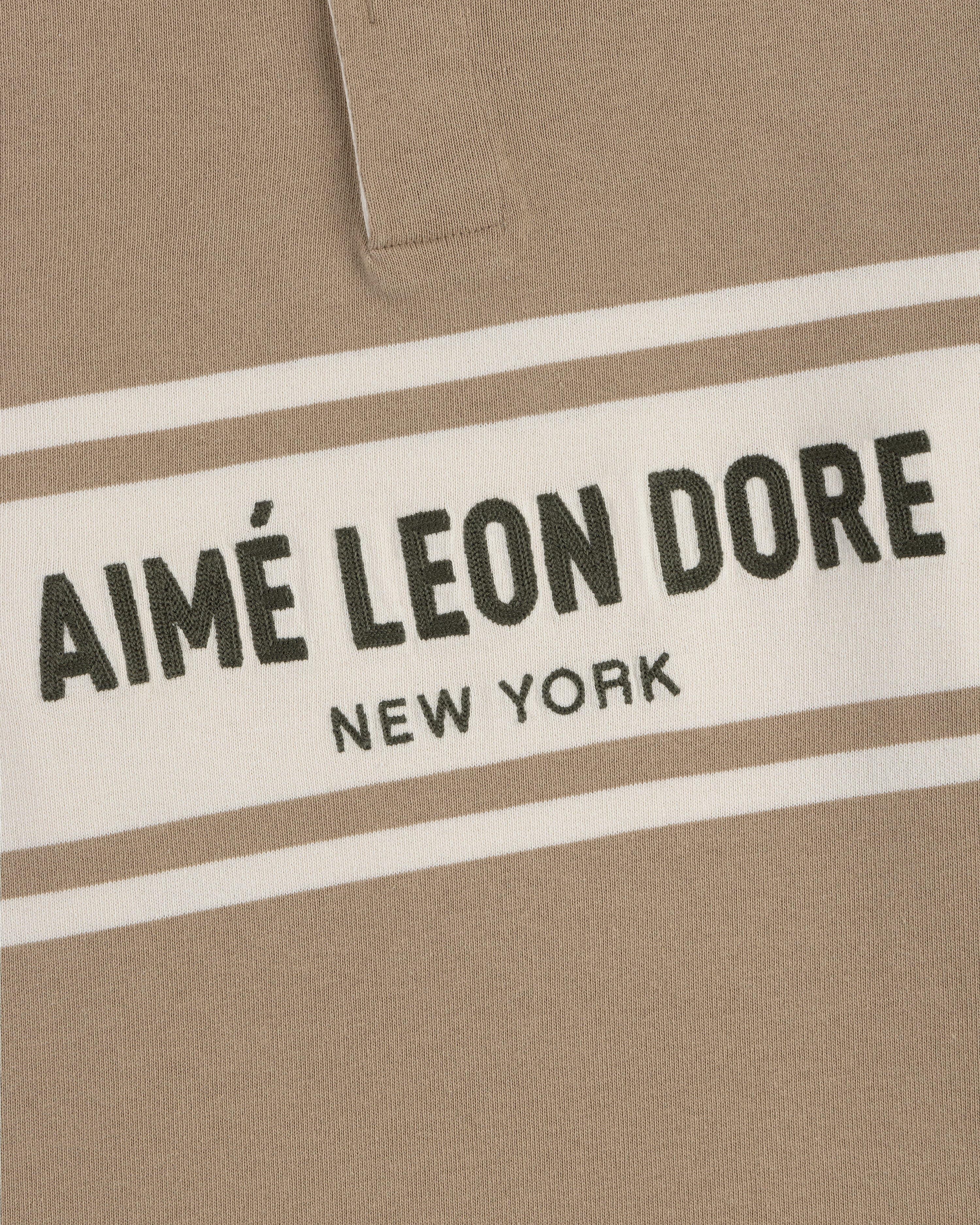 Close-up of a beige Chest Stripe Logo Rugby with AIMÉ LEON DORE NEW YORK in bold black on a white chest stripe.