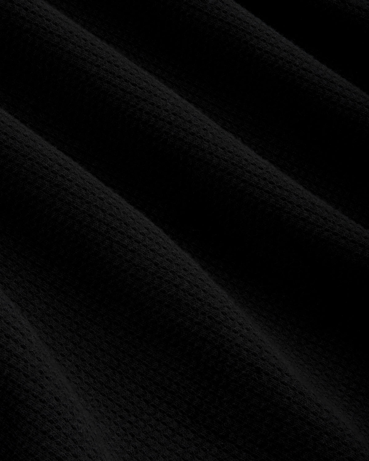 Black mesh muscle tank with diagonal folds, creating shadows and a subtle waffle texture across the surface.