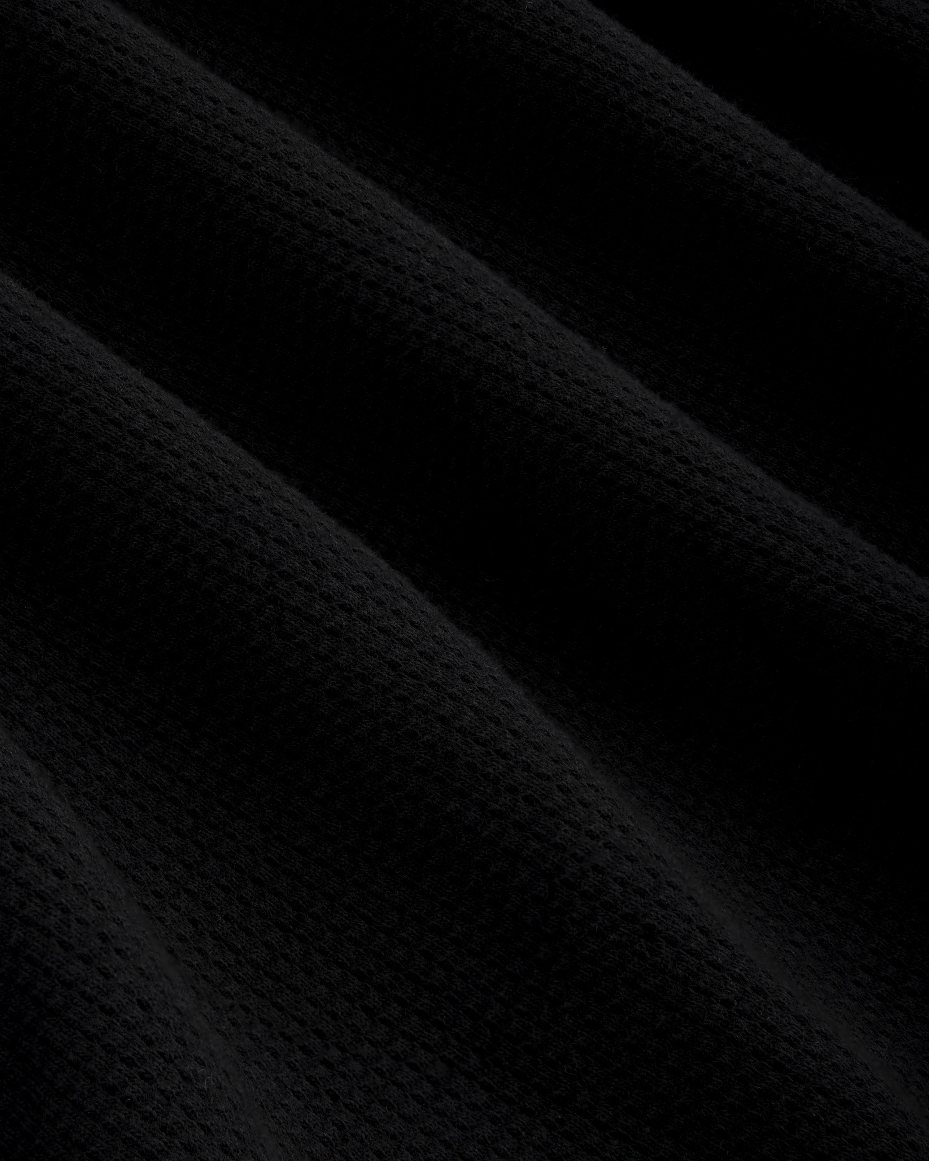 Black mesh muscle tank with diagonal folds, creating shadows and a subtle waffle texture across the surface.