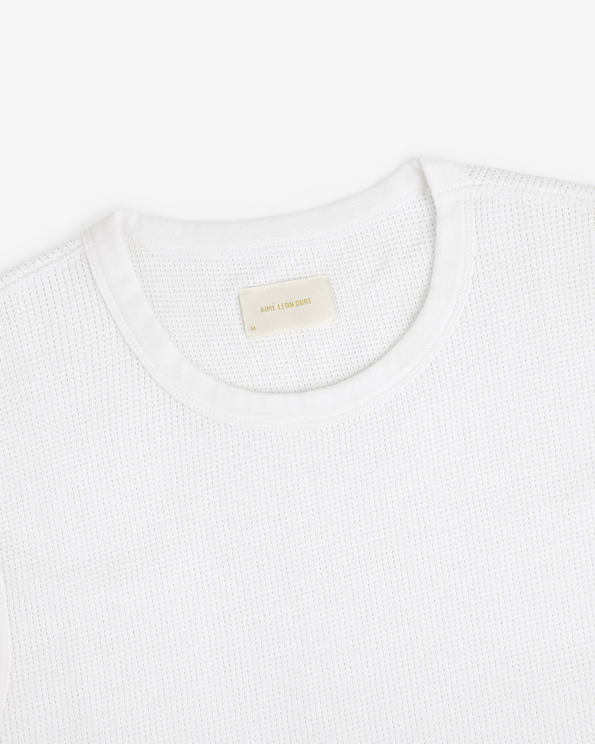 A close-up of a white Mesh Muscle Tank with a beige label inside the collar.
