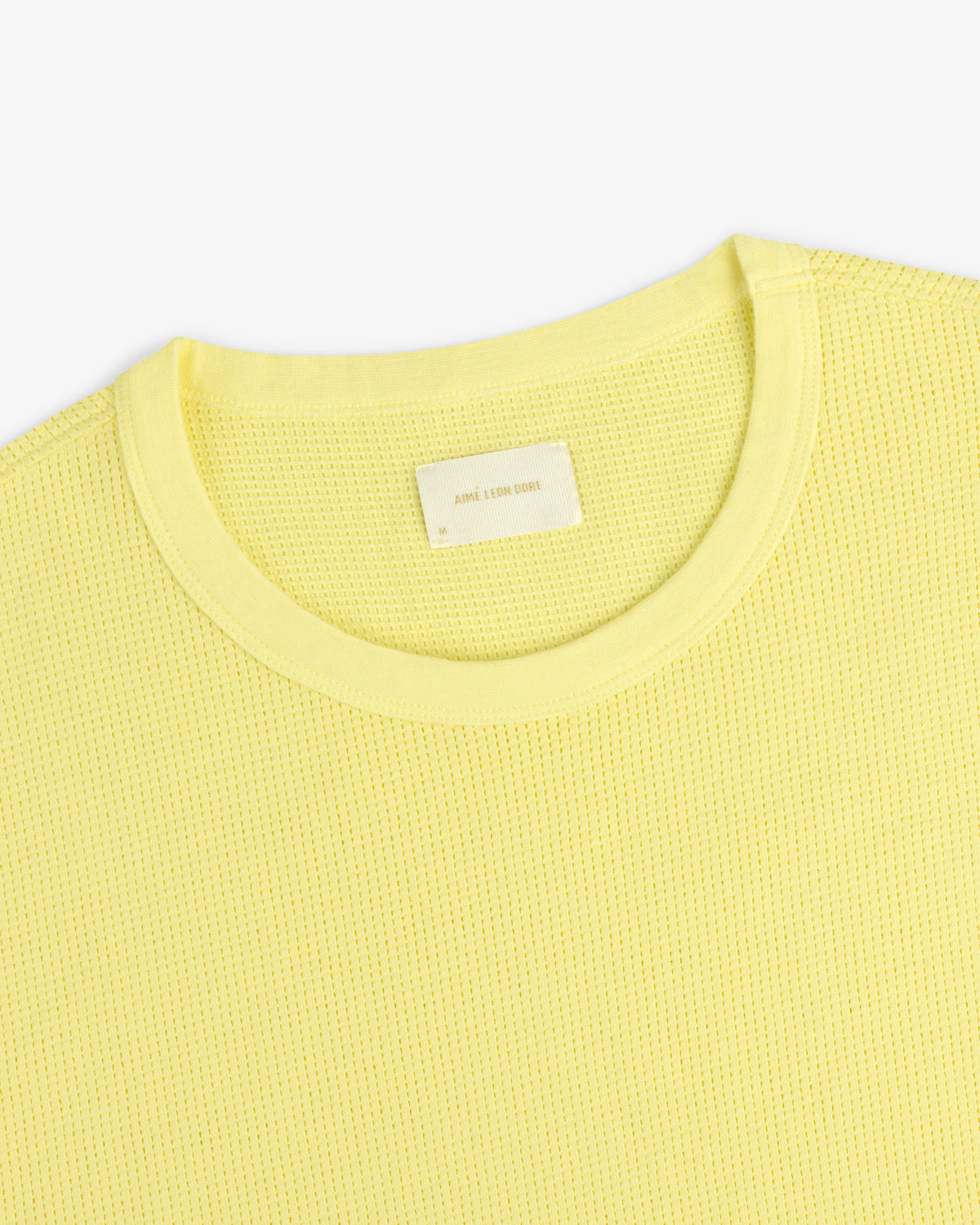 A close-up of a light yellow Mesh Muscle Tank with a blank neck label on a plain background.