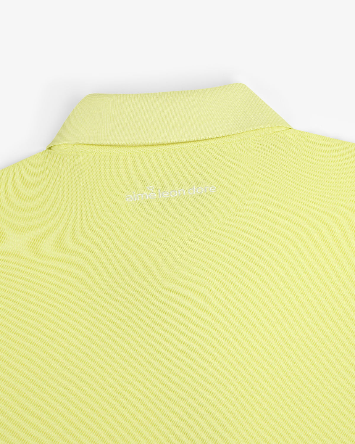 A close-up of the back collar of the light yellow ALD Golf Polo with "alml éean done" printed in white.