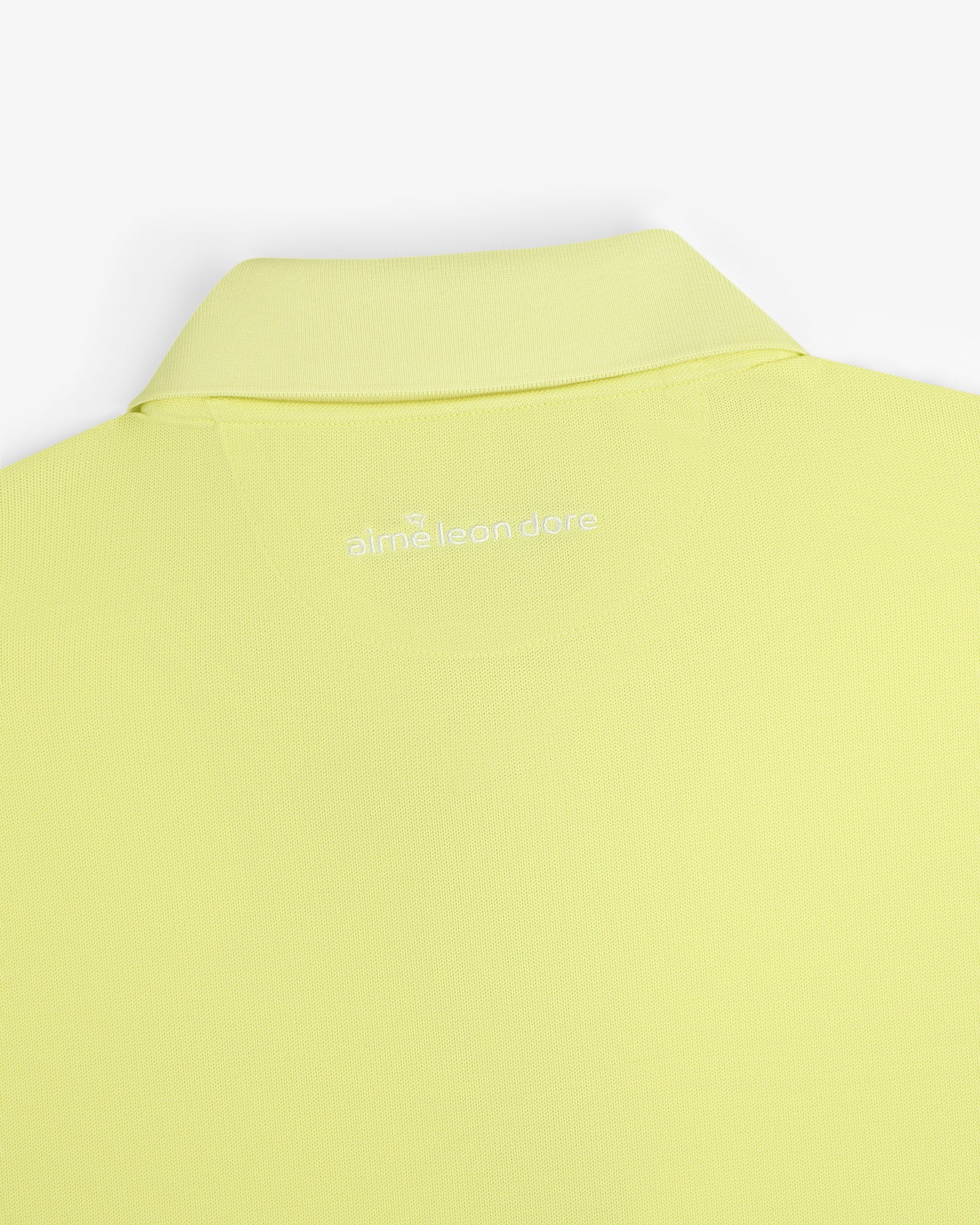 A close-up of the back collar of the light yellow ALD Golf Polo with "alml éean done" printed in white.