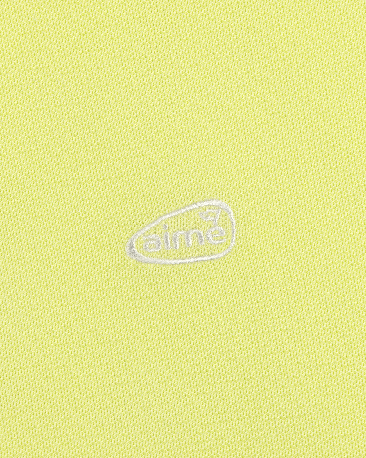Light yellow ALD Golf Polo featuring textured fabric and an oval-shaped white aimé logo embroidered at the center.