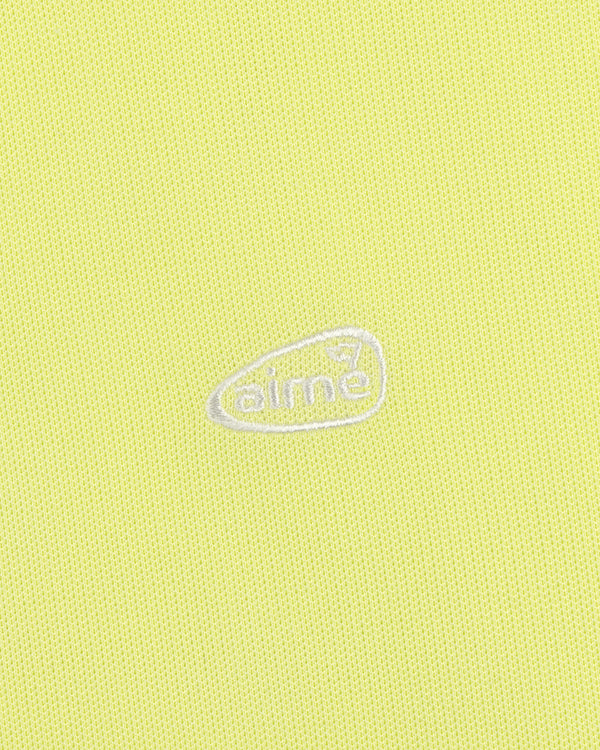 Light yellow ALD Golf Polo featuring textured fabric and an oval-shaped white aimé logo embroidered at the center.