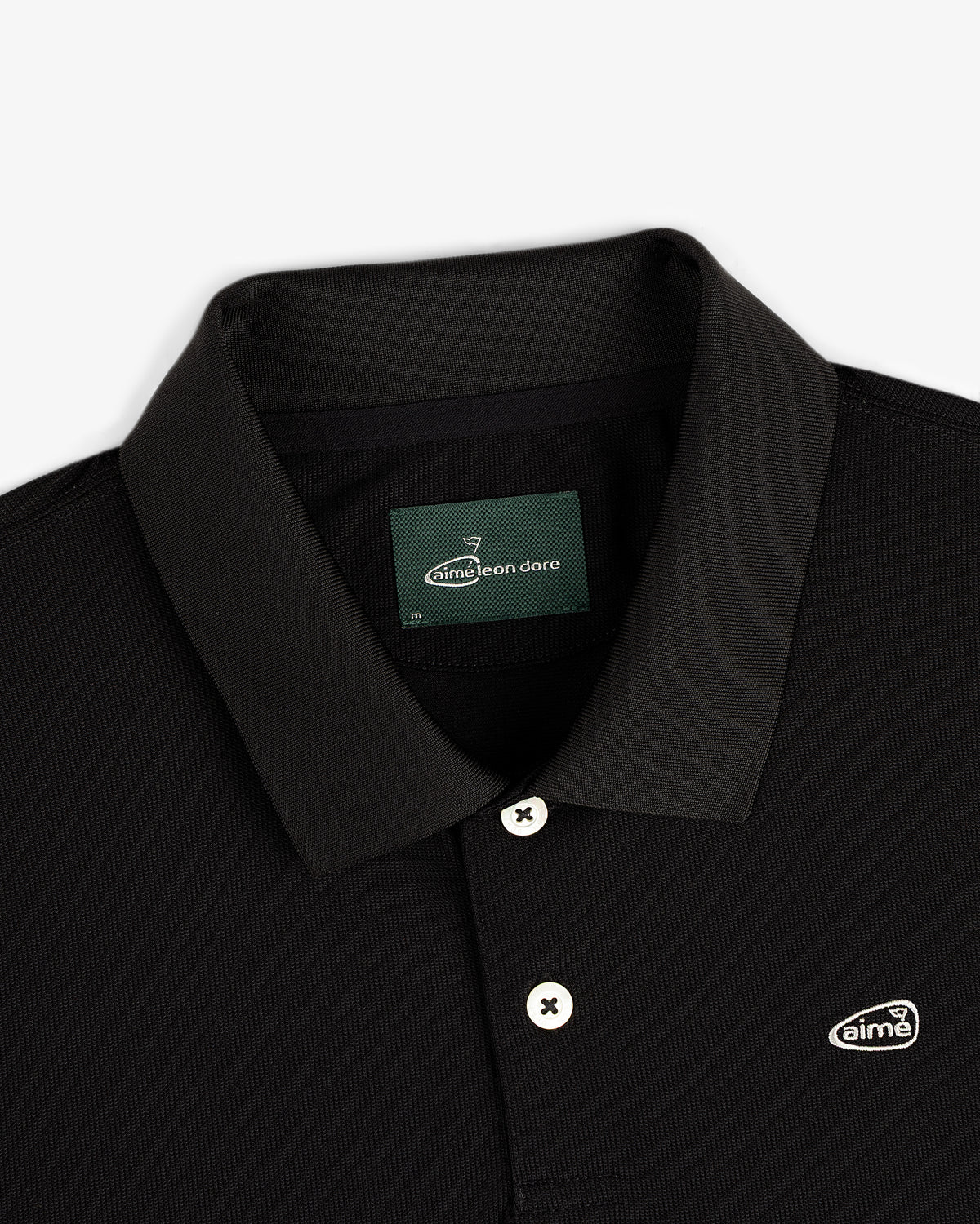 Close-up of the ALD Golf Polo, a black collared shirt with white buttons and a small Aimé Leon Dore chest logo patch.