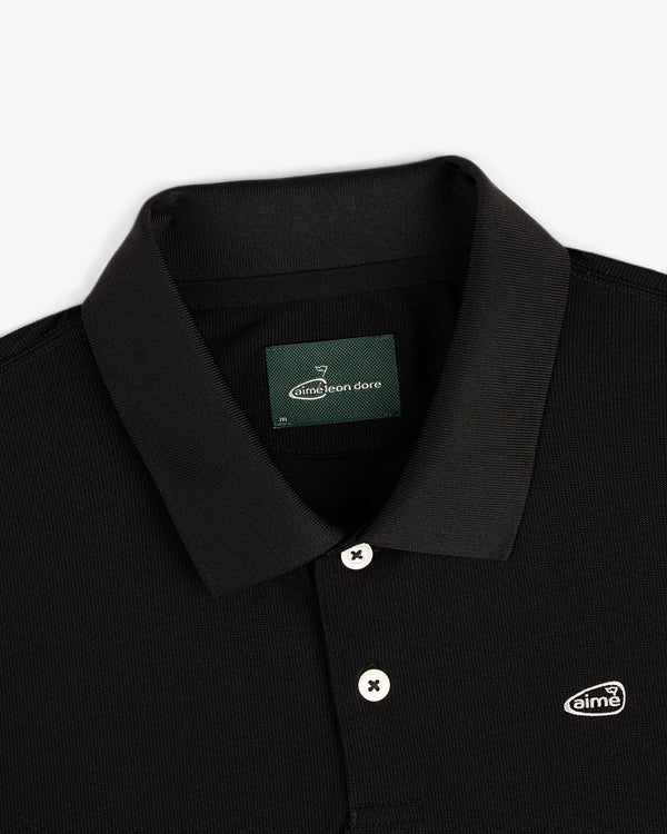 Close-up of the ALD Golf Polo, a black collared shirt with white buttons and a small Aimé Leon Dore chest logo patch.