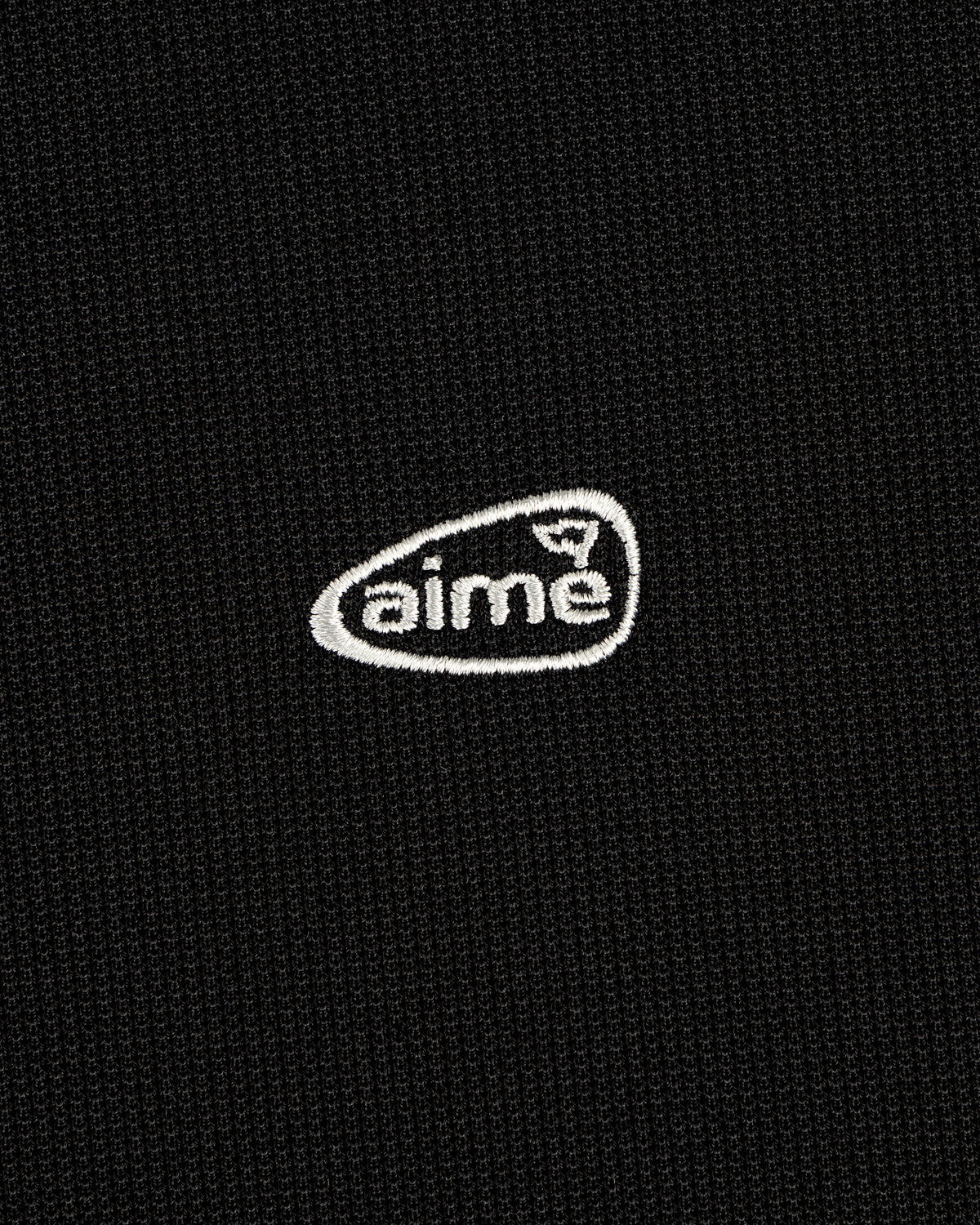 Black textured ALD Golf Polo with small white "aime" logo embroidered inside an irregular oval.