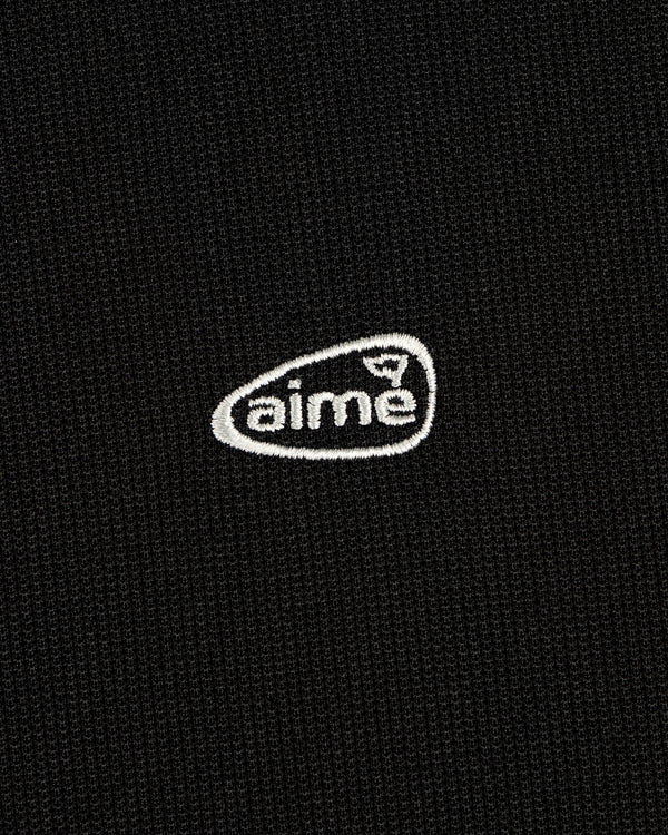 Black textured ALD Golf Polo with small white "aime" logo embroidered inside an irregular oval.