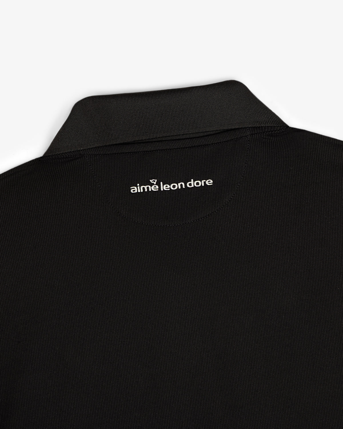 Close-up of an ALD Golf Polo’s black collar with aime leon dore text printed in white below the back neckline.