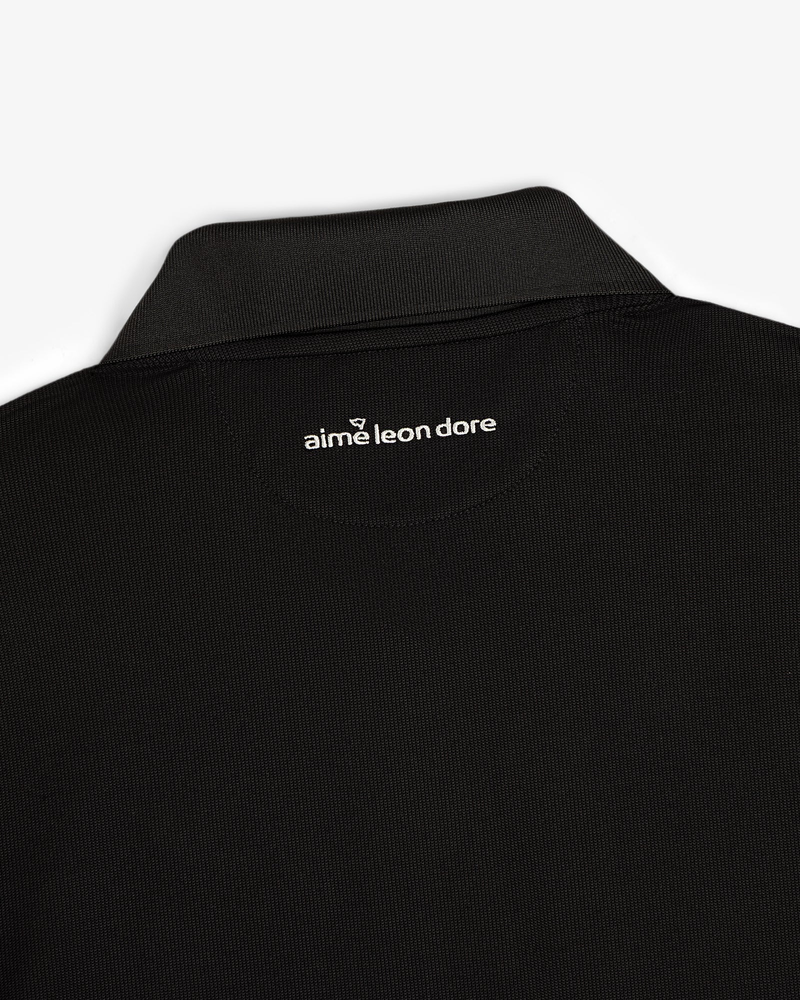 Close-up of an ALD Golf Polo’s black collar with aime leon dore text printed in white below the back neckline.