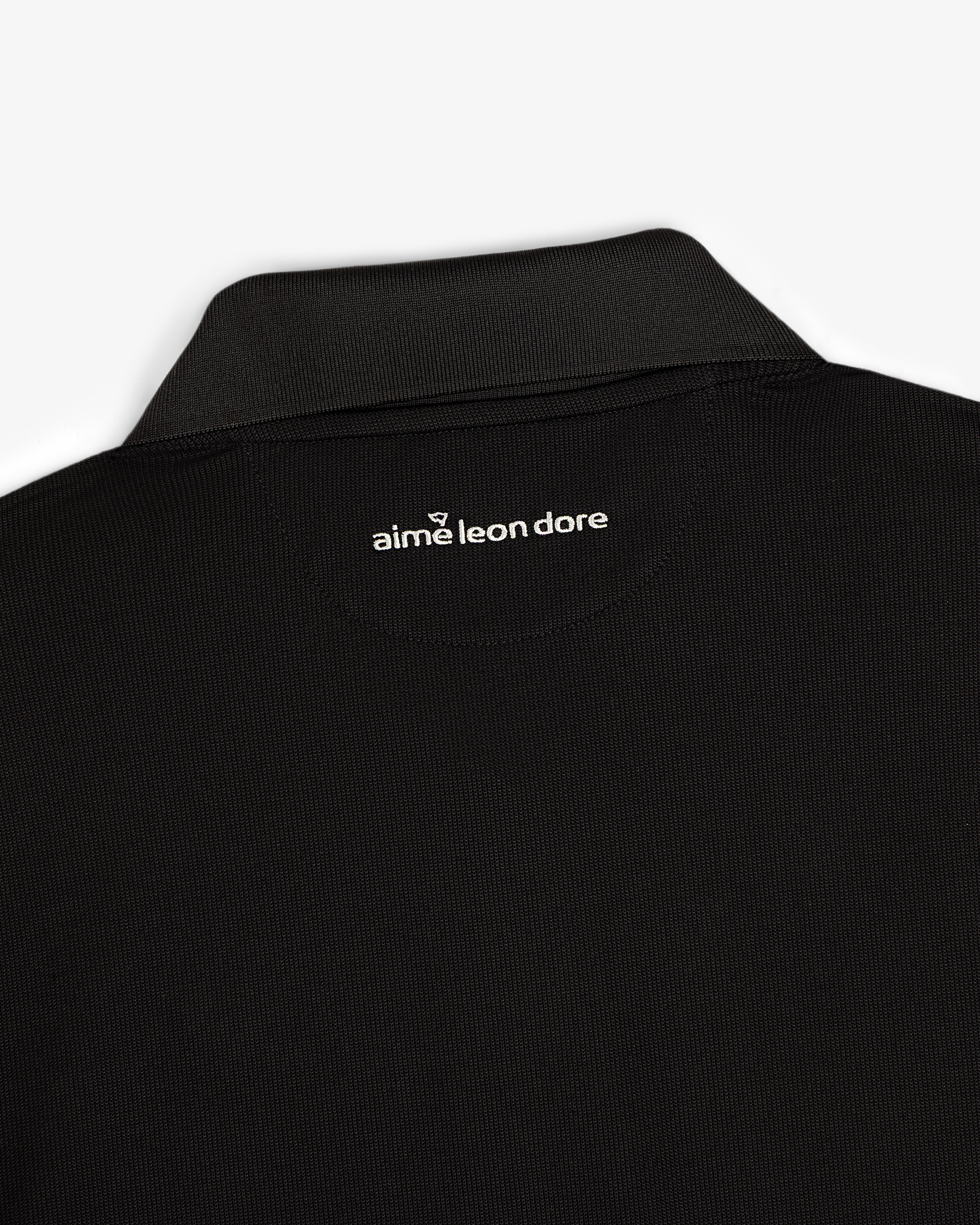Close-up of an ALD Golf Polo’s black collar with aime leon dore text printed in white below the back neckline.