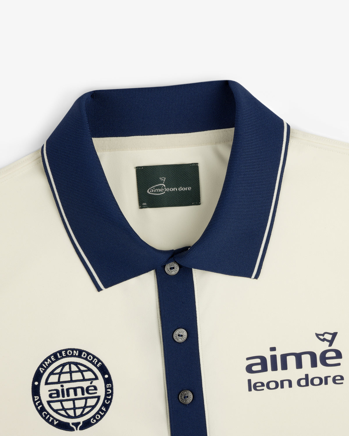 ALD Golf Tour Polo: Cream shirt with navy collar, logo, and “All City Golf Club” globe emblem on the chest.