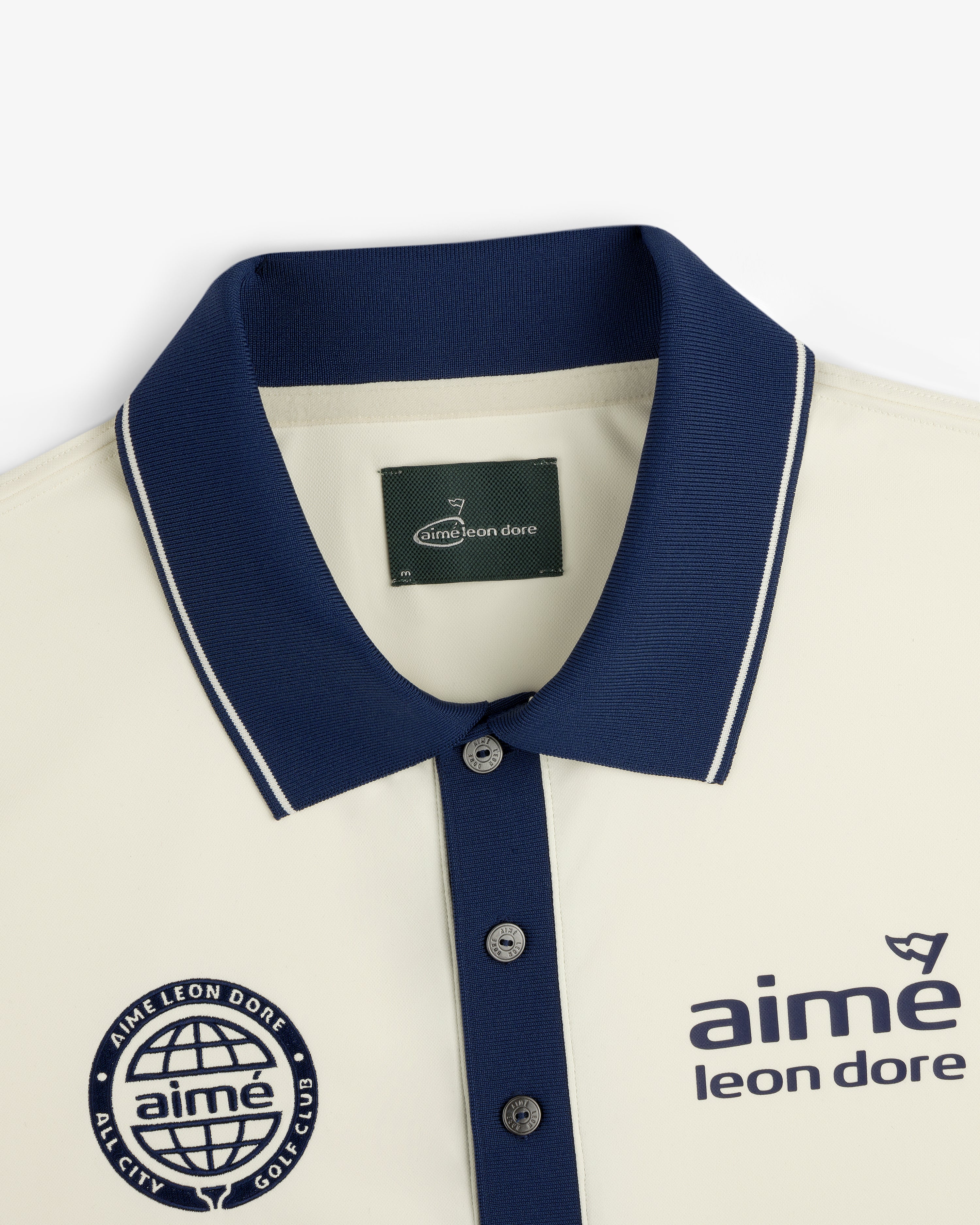 ALD Golf Tour Polo: Cream shirt with navy collar, logo, and “All City Golf Club” globe emblem on the chest.