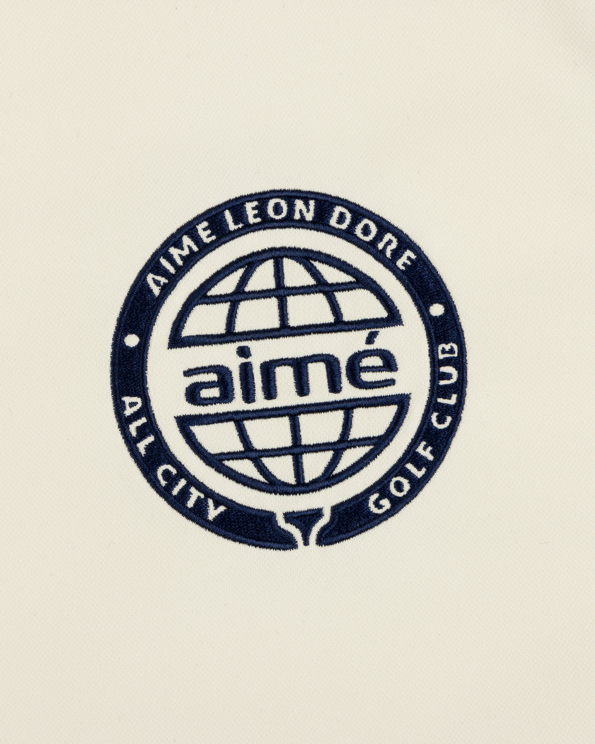 Navy blue ALD Golf Tour Polo with All City Golf Club globe logo and "aimé" on a cream background.