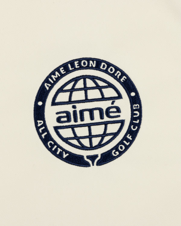 Navy blue ALD Golf Tour Polo with All City Golf Club globe logo and "aimé" on a cream background.