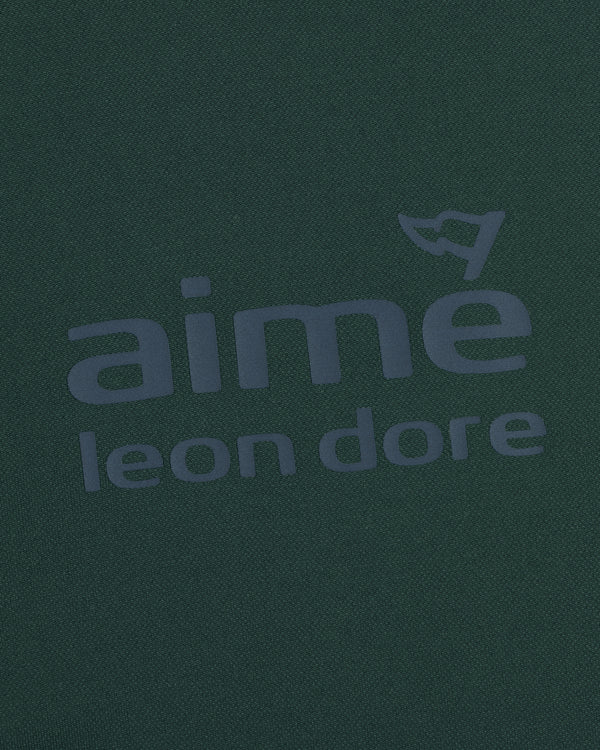 Close-up of the ALD Golf Tour Polo’s dark green fabric with bold aimé leon dore text and a flag graphic above the "e".