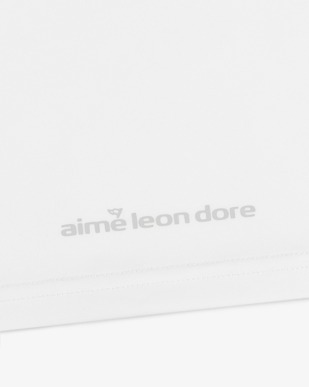 Close-up of a white ALD Golf Performance Tee with the aime leon dore logo in light gray near the bottom hem.