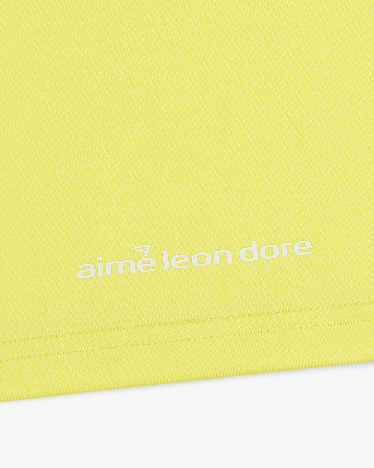 Close-up of the ALD Golf Performance Tee in yellow with the aime leon dore logo printed in white near the hem.