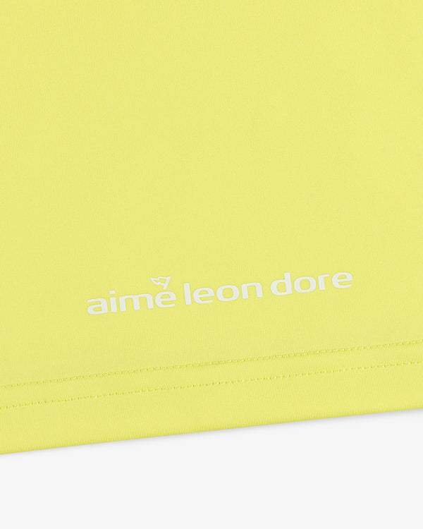 Close-up of the ALD Golf Performance Tee in yellow with the aime leon dore logo printed in white near the hem.