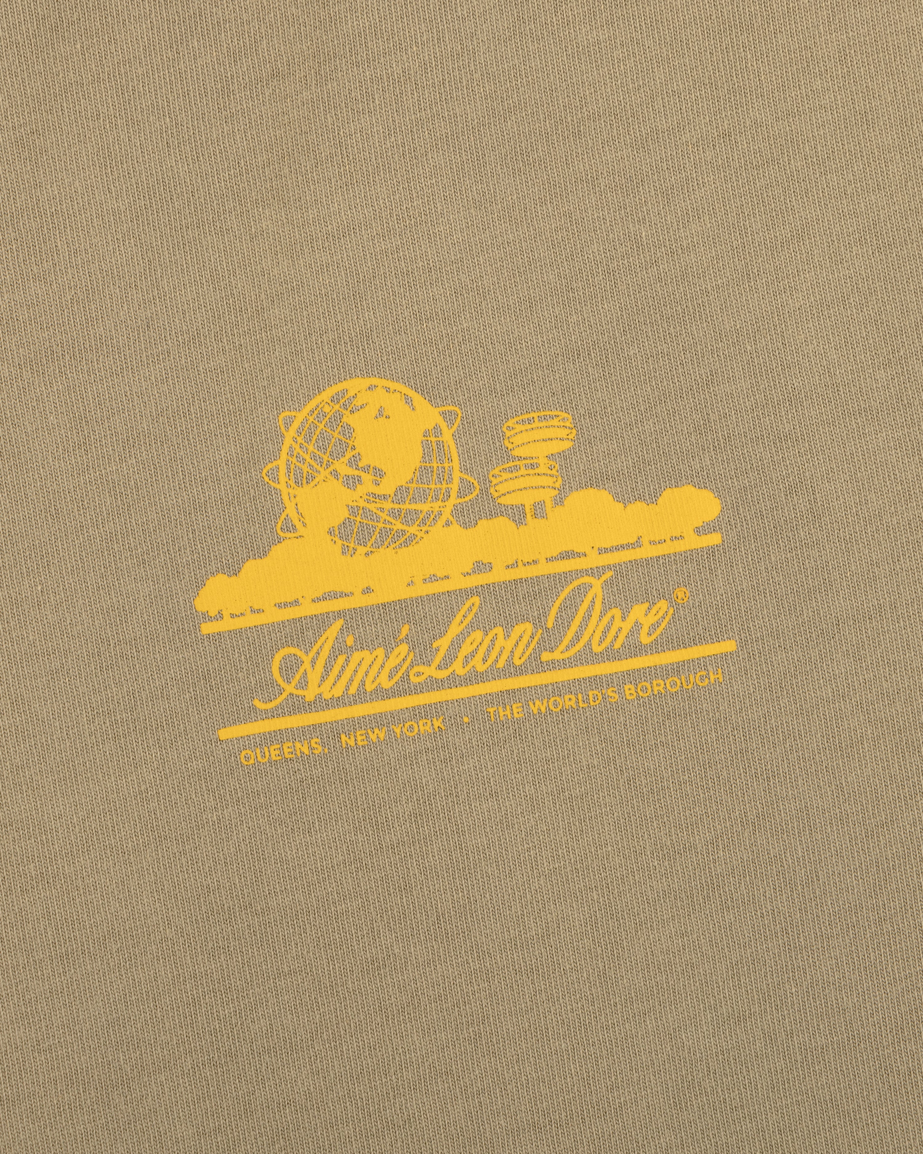 Tan Sun Faded Unisphere Tee with yellow globe and buildings graphic, Aimé Leon Dore text, and Queens, New York.