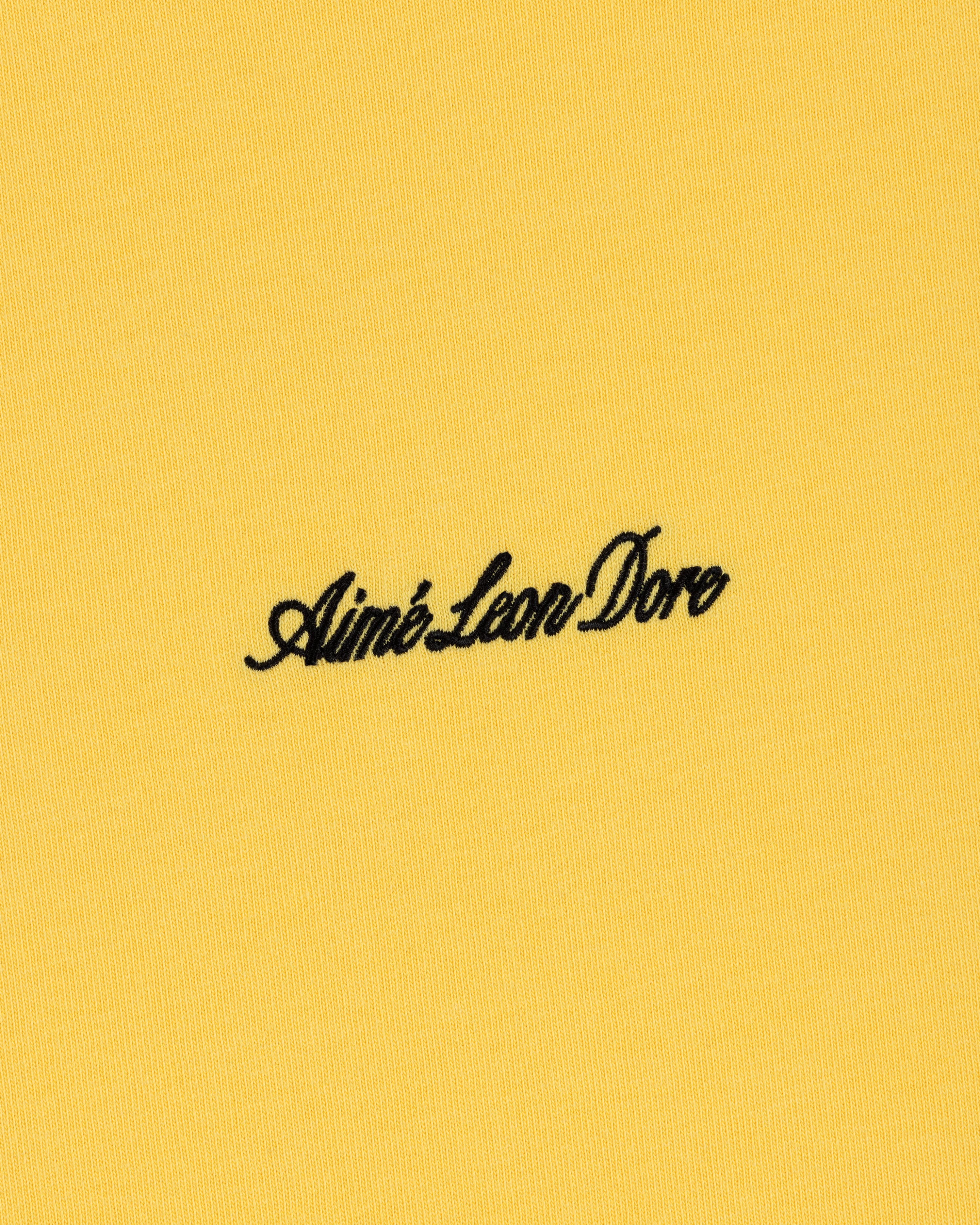 Black Aimé Leon Dore script logo embroidered on yellow Embroidered Logo Tee.