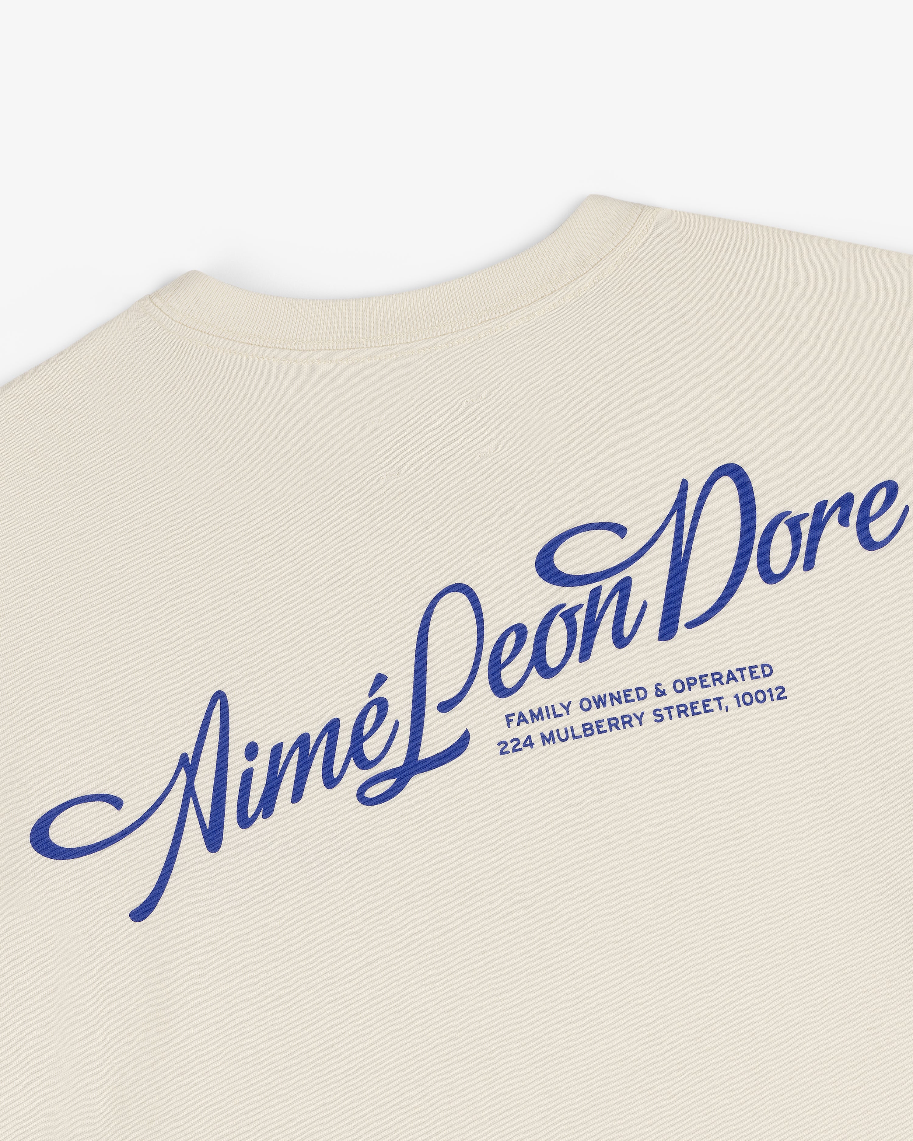 Pappoús Logo Tee: Beige shirt with large blue Aimé Leon Dore script and 224 Mulberry Street, 10012 on back.