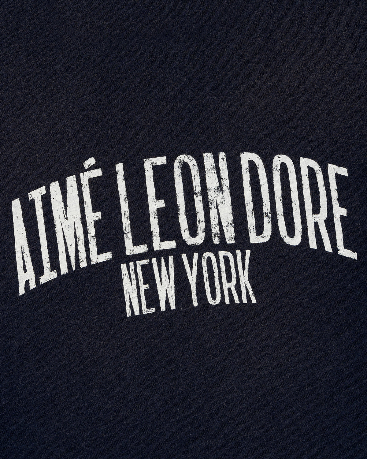 White, distressed "AIMÉ LEON DORE NEW YORK" text on the Washed Ringer Tee's dark fabric background.