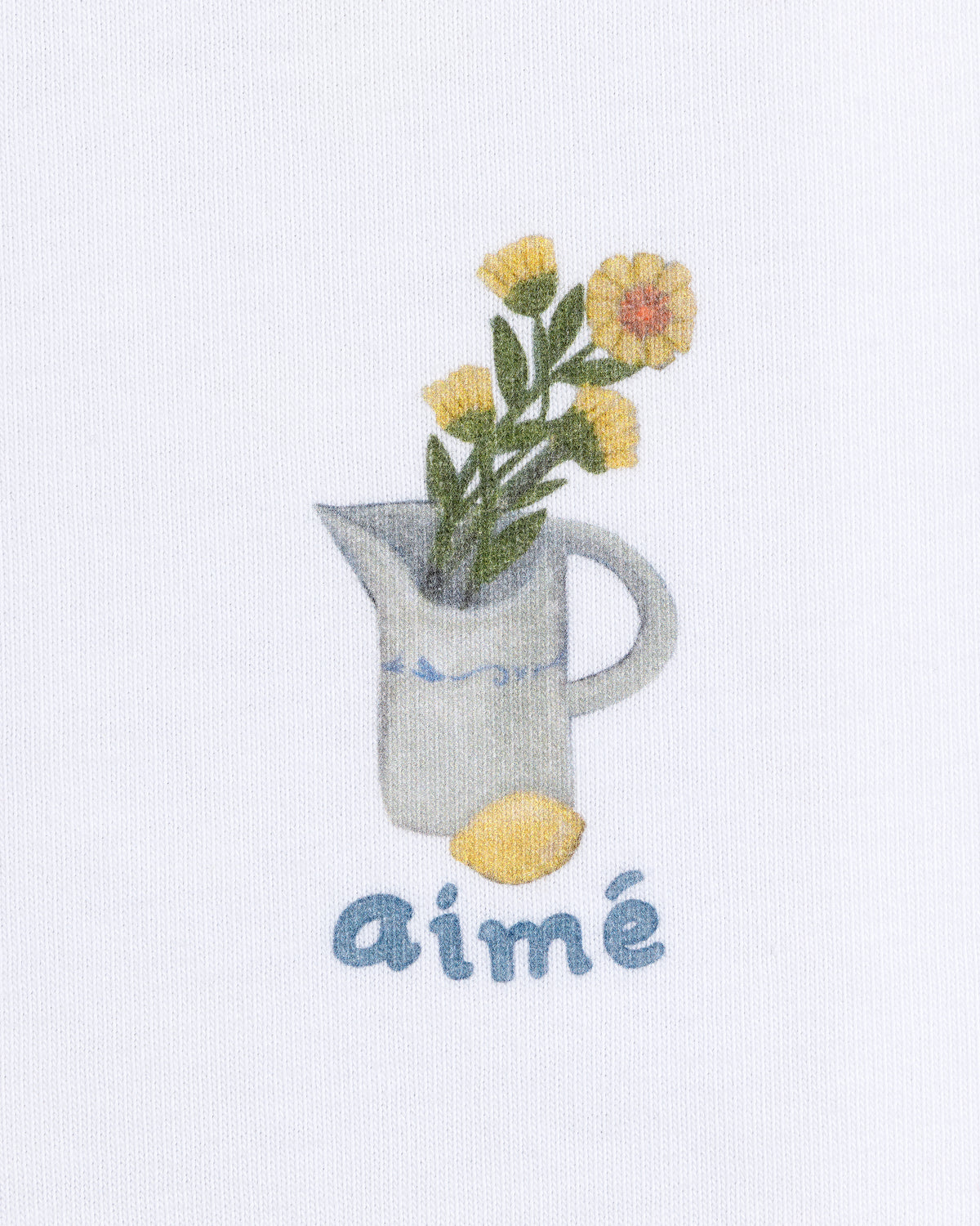 The Breakfast Tee features a white pitcher with yellow flowers, a lemon, and "aimé" in blue text below.